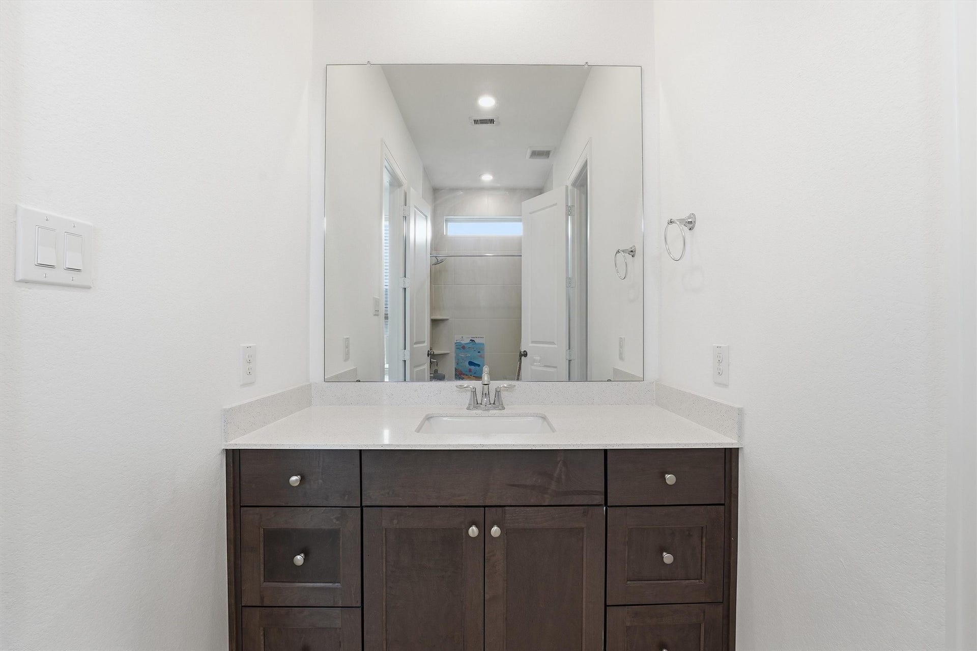 Elegant bathroom with a sleek quartz countertop, dark wood cabinetry, and a large mirror enhancing the space.