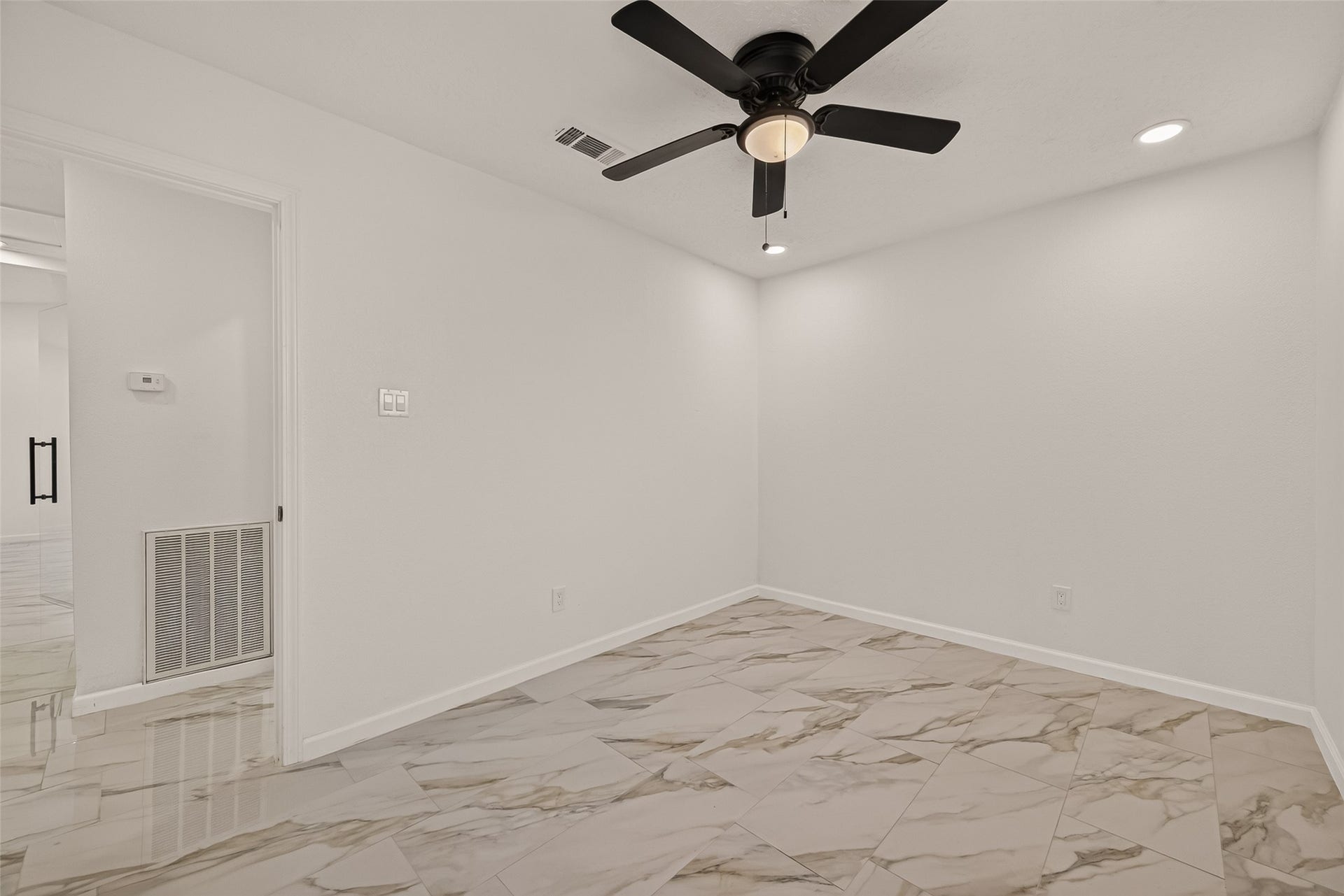 16619 Tibet Road, Friendswood, TX 77546 This room features a clean, modern design with neutral walls, marble-patterned tile flooring, and a ceiling fan. Recessed lighting adds brightness, and the open doorway leads to the adjacent space, enhancing the room's airy feel.
