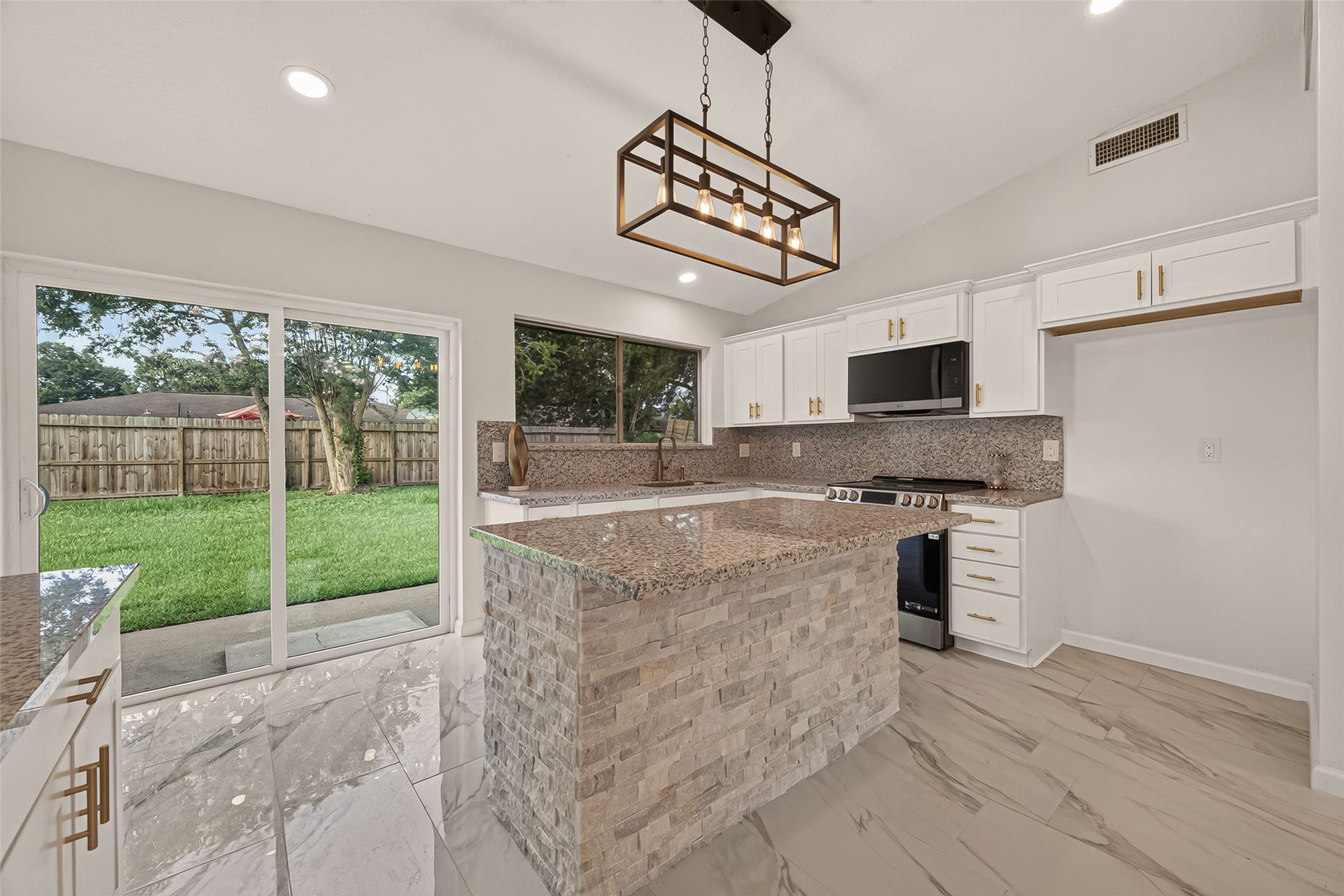 16619 Tibet Road, Friendswood, TX 77546 This modern kitchen features sleek white cabinetry, granite countertops, and a stylish stone island. It boasts stainless steel appliances, recessed lighting, and a large window for natural light. The space opens up to a backyard view through sliding glass doors, offering a seamless indoor-outdoor flow.