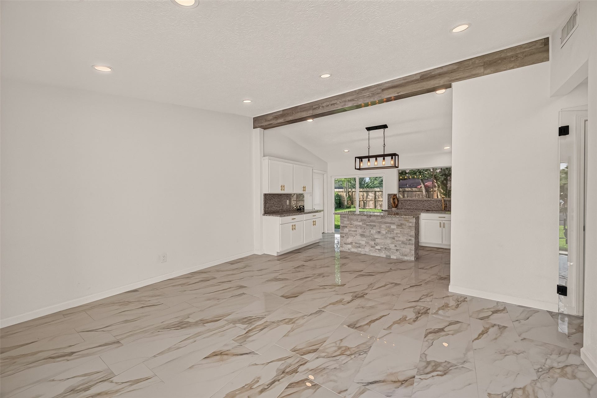 16619 Tibet Road, Friendswood, TX 77546 This modern home features an open-concept layout with sleek, glossy marble floors and recessed lighting. The spacious kitchen boasts a central island with a stone finish, white cabinetry, and large windows offering plenty of natural light.