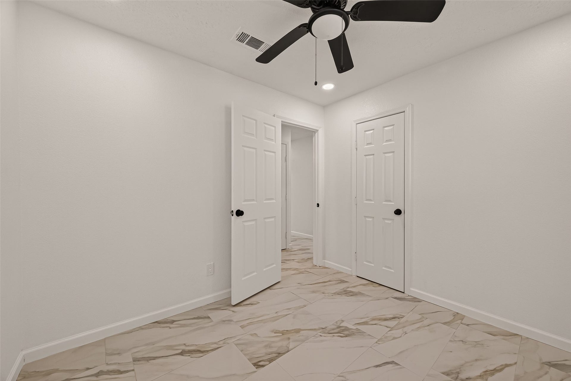 16619 Tibet Road, Friendswood, TX 77546 Bright, modern room with sleek marble-patterned tile flooring, neutral walls, and a ceiling fan. Featuring two white doors, it's a versatile space perfect for a bedroom or office.