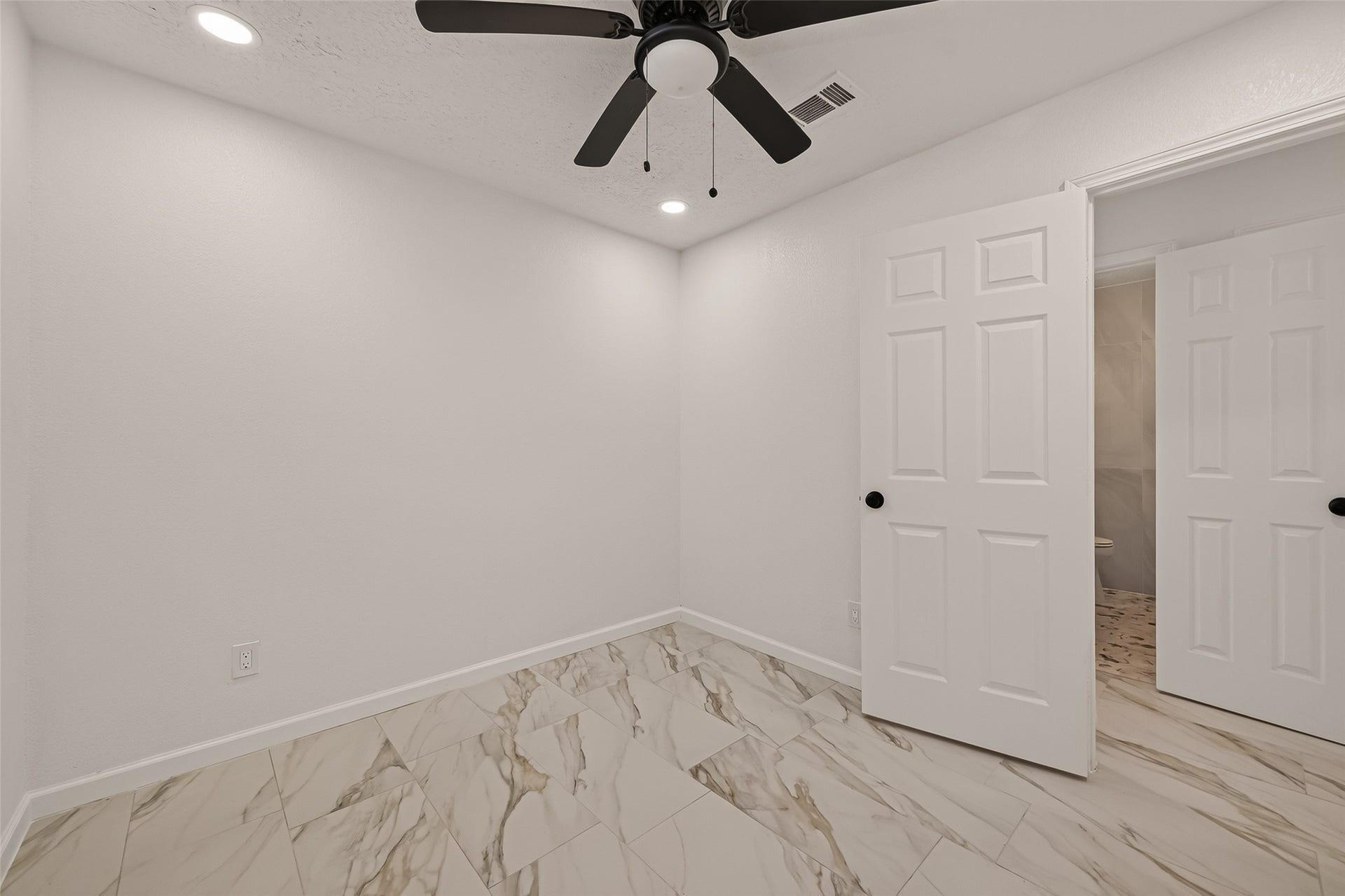 16619 Tibet Road, Friendswood, TX 77546 This room features clean white walls, marble-patterned tile flooring, and a ceiling fan with light. A partially open door reveals an adjacent space, offering a modern and neutral setting.
