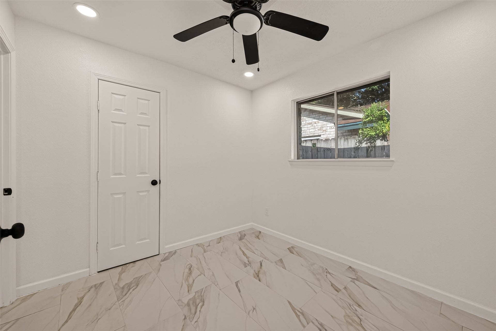 16619 Tibet Road, Friendswood, TX 77546 This room features sleek marble-patterned flooring, a ceiling fan, and a window offering natural light. The white walls and ceiling create a fresh, modern look, while the interior door complements the clean design.