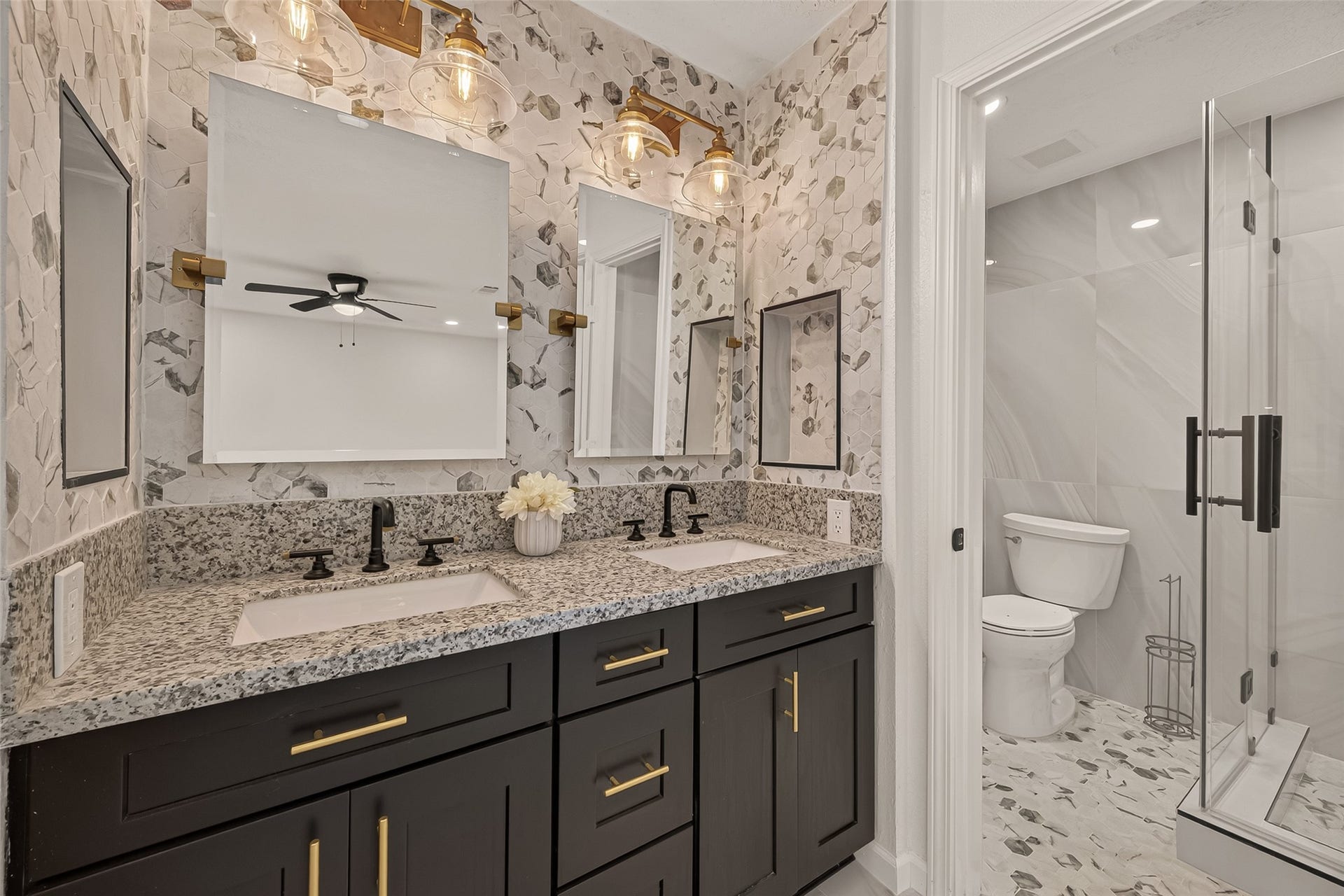 16619 Tibet Road, Friendswood, TX 77546 This bathroom features a modern design with a dual-sink vanity, granite countertops, and stylish black fixtures. The space includes a separate glass-enclosed shower and a toilet area with elegant tile work.