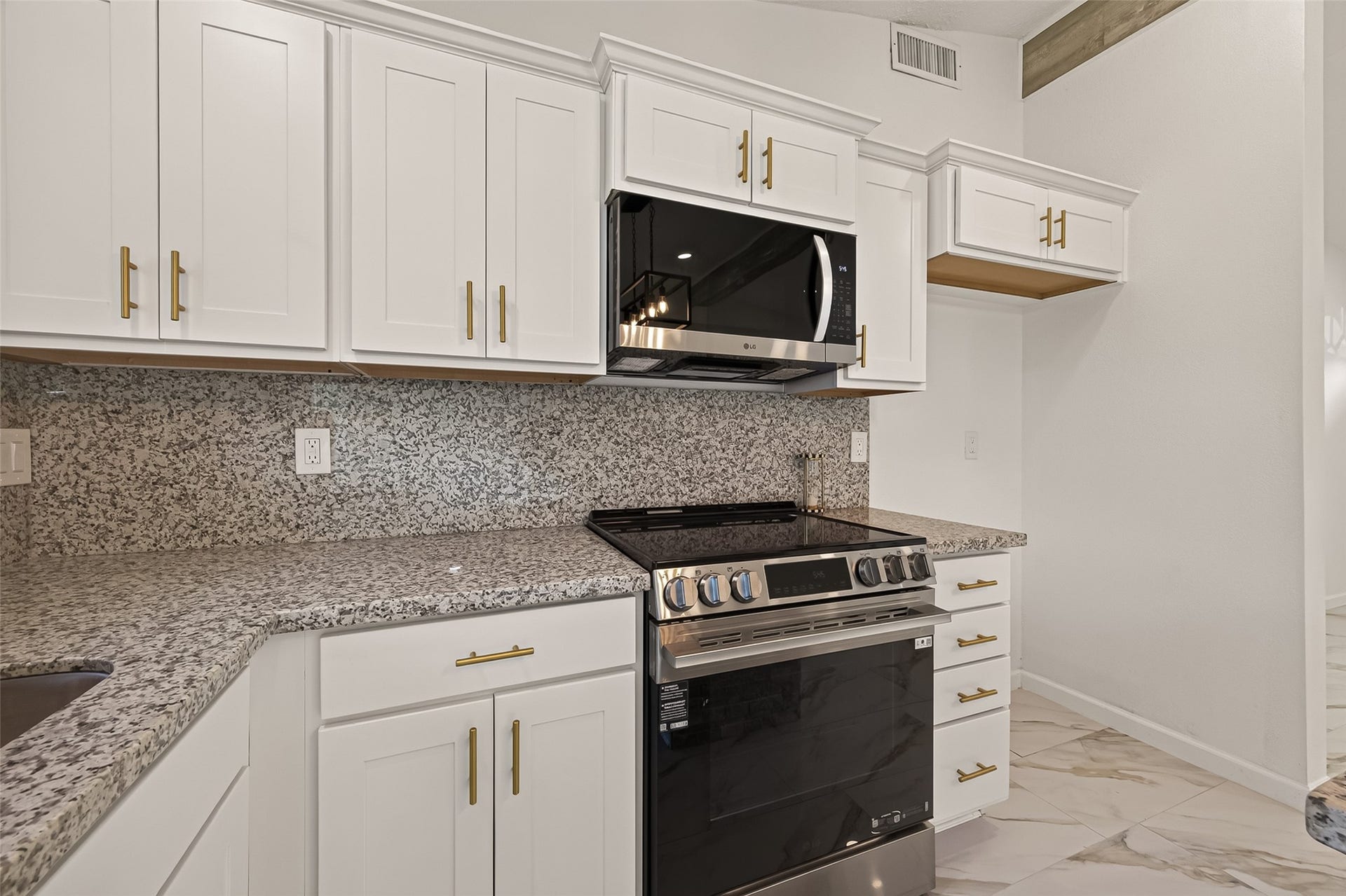 16619 Tibet Road, Friendswood, TX 77546 This kitchen features modern white cabinetry with sleek gold handles, a stylish granite countertop, and a stainless steel oven and microwave. The clean design offers a contemporary feel, ideal for a modern home.