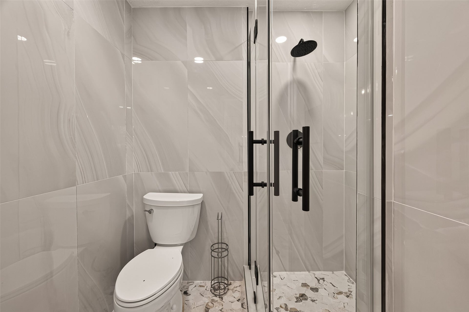 16619 Tibet Road, Friendswood, TX 77546 Modern bathroom featuring sleek, large-format tiles, a glass-enclosed shower with black fixtures, and a contemporary toilet. The space is well-lit and elegant, offering a clean, sophisticated look.