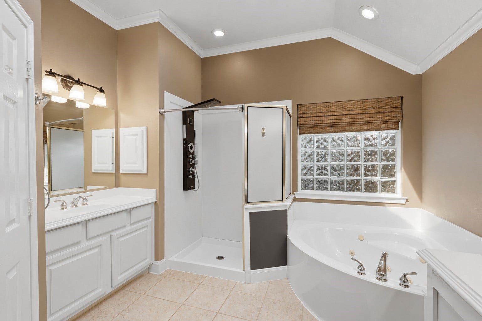 The primary bath offers a corner jetted soaking tub, separate shower, expansive vanity, large mirror, and vaulted ceiling.