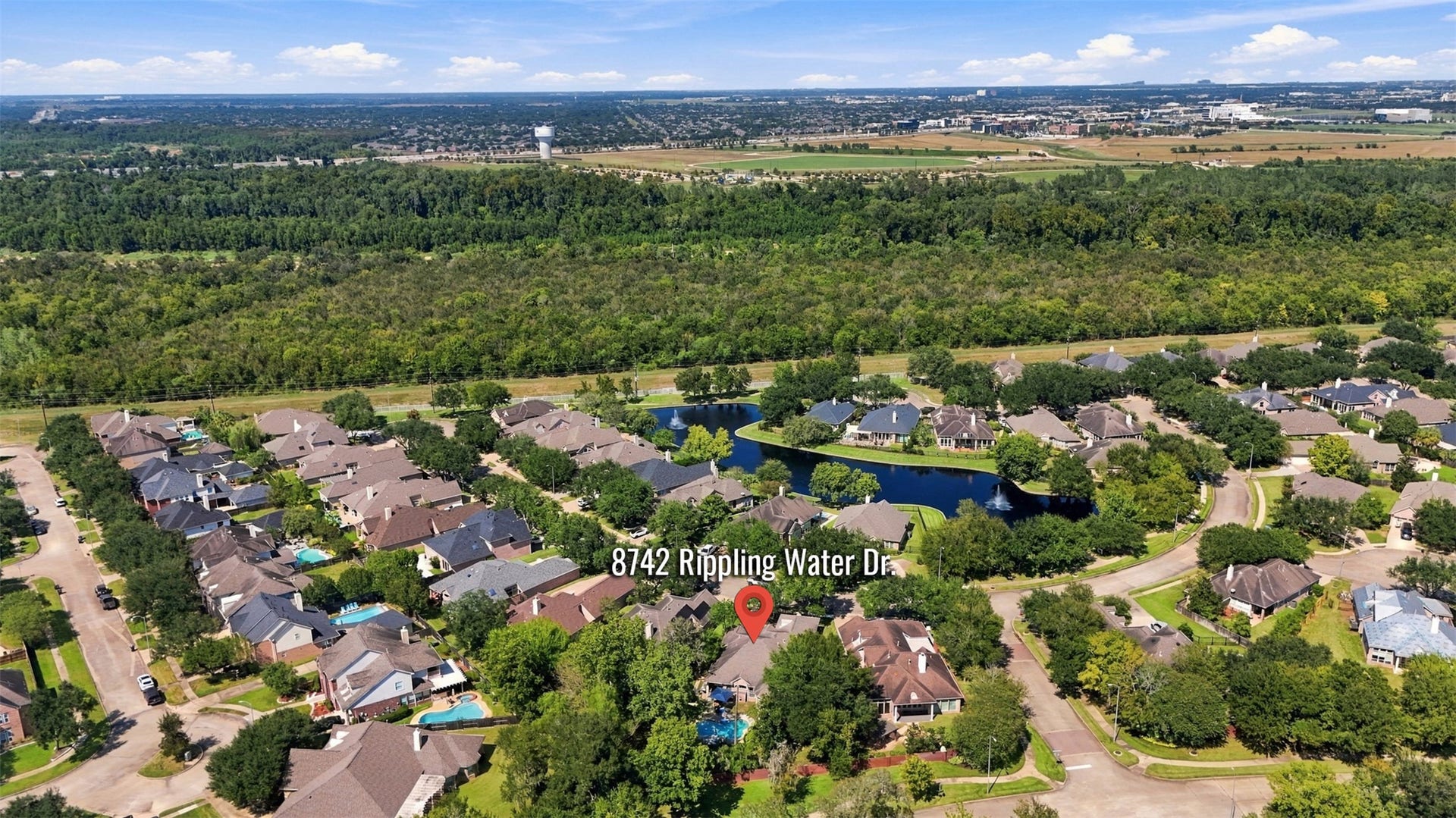A wider aerial view showcases Greatwoods residential setting, nearby lakes, mature landscaping, and the broader Sugar Land area surrounding the property.
