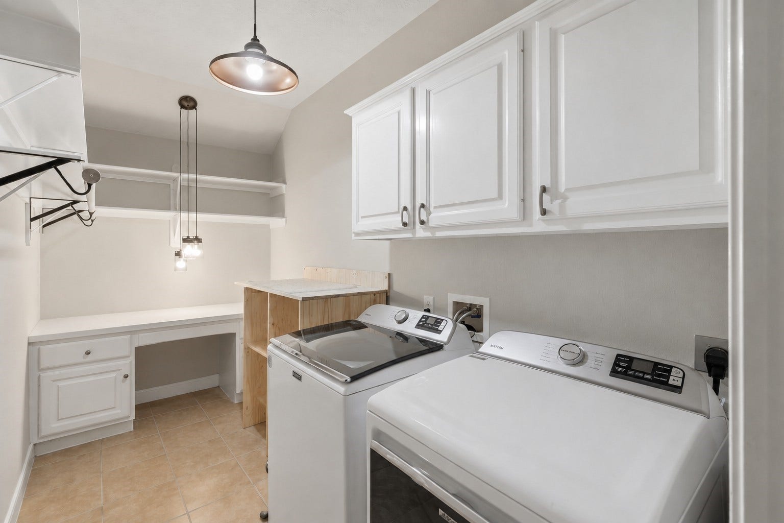The dedicated utility room features generous cabinetry, built-in workspace, open shelving, and space for a side-by-side washer and dryer.