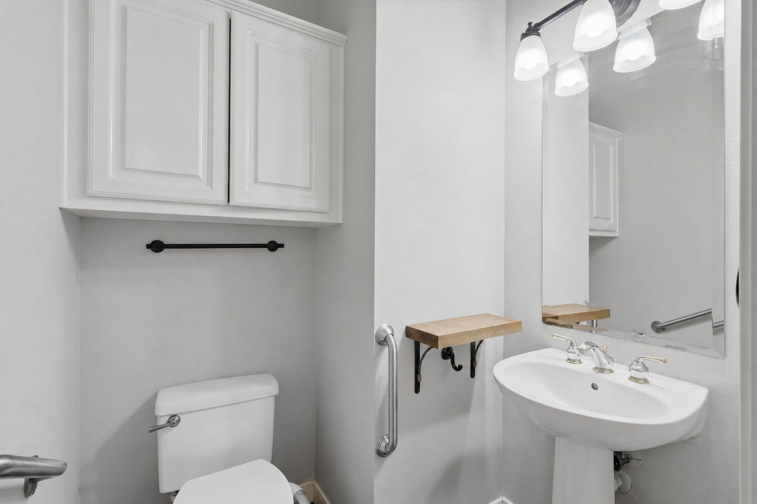 The powder bath includes a pedestal sink, overhead cabinetry, large mirror, and conveniently placed grab bars.