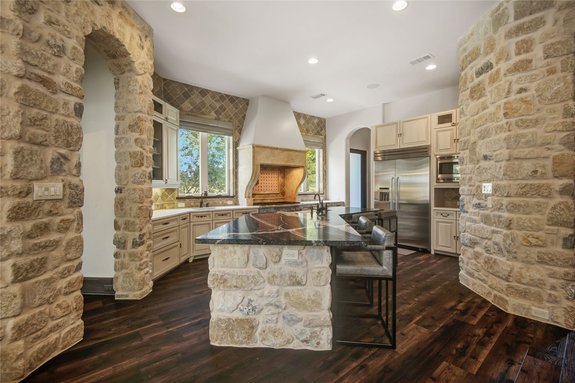10 Sullivans Lane, Missouri City, TX 77459 Kitchen features rustic stone walls and dark wood flooring, creating a warm, inviting atmosphere. It includes modern stainless steel appliances, a spacious island with seating, and ample cabinetry for storage.