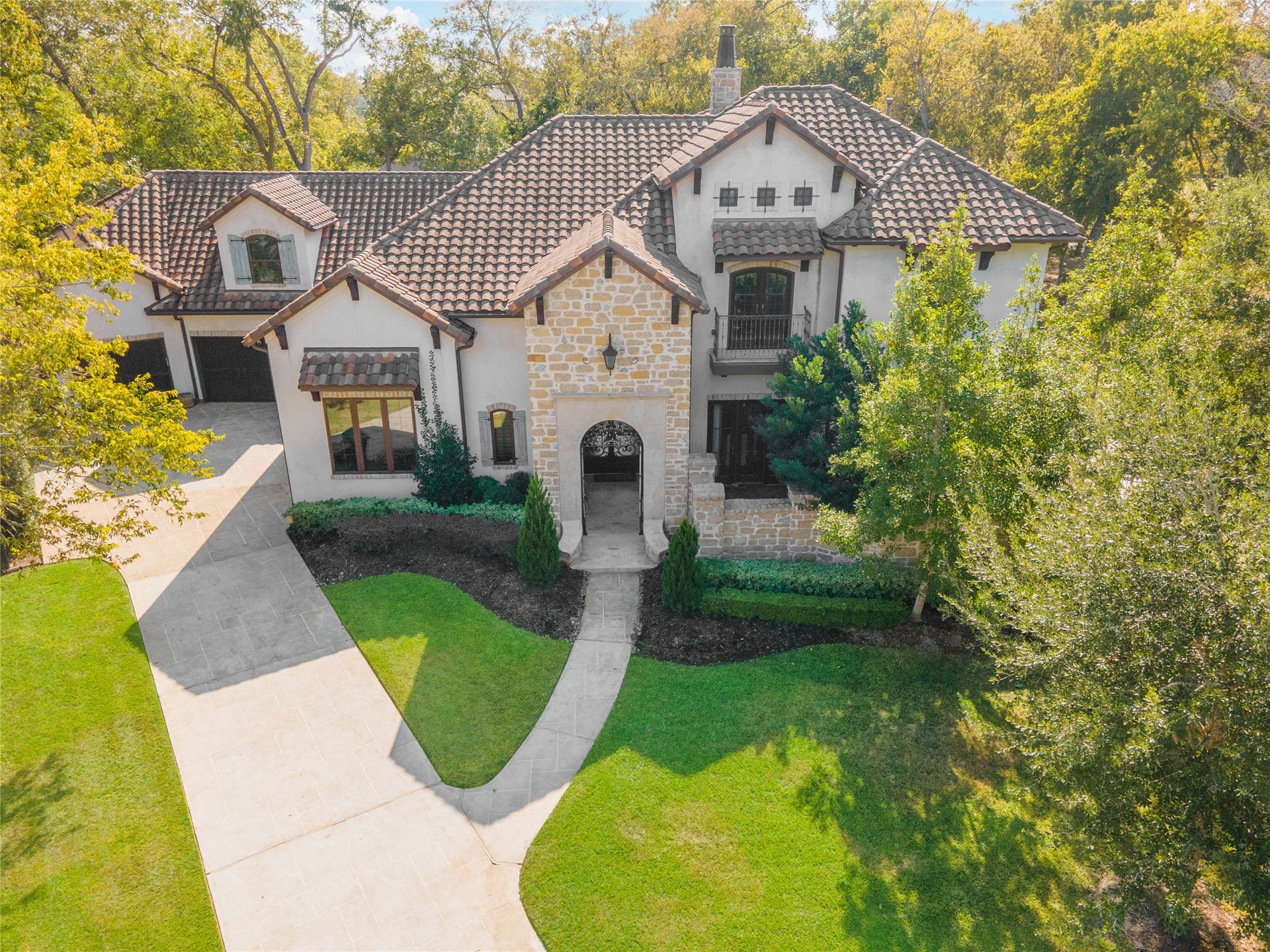 10 Sullivans Lane, Missouri City, TX 77459 Aerial view of this elegant two-story home featuring a charming stone faade, a classic tile roof, and a welcoming arched entryway.