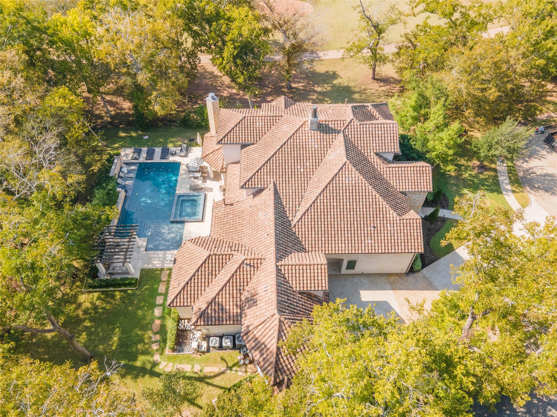 10 Sullivans Lane, Missouri City, TX 77459 This aerial view showcases the terracotta-tiled roof, nestled among mature trees. The property features a luxurious backyard with a large swimming pool, hot tub, and a patio area perfect for relaxation and entertaining.