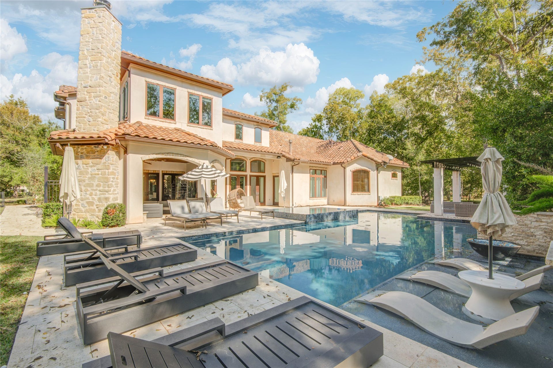 10 Sullivans Lane, Missouri City, TX 77459 Stunning, luxurious outdoor space. The backyard boasts a sparkling pool surrounded by stylish lounge chairs and a cozy patio area, perfect for entertaining and relaxation amidst lush greenery.