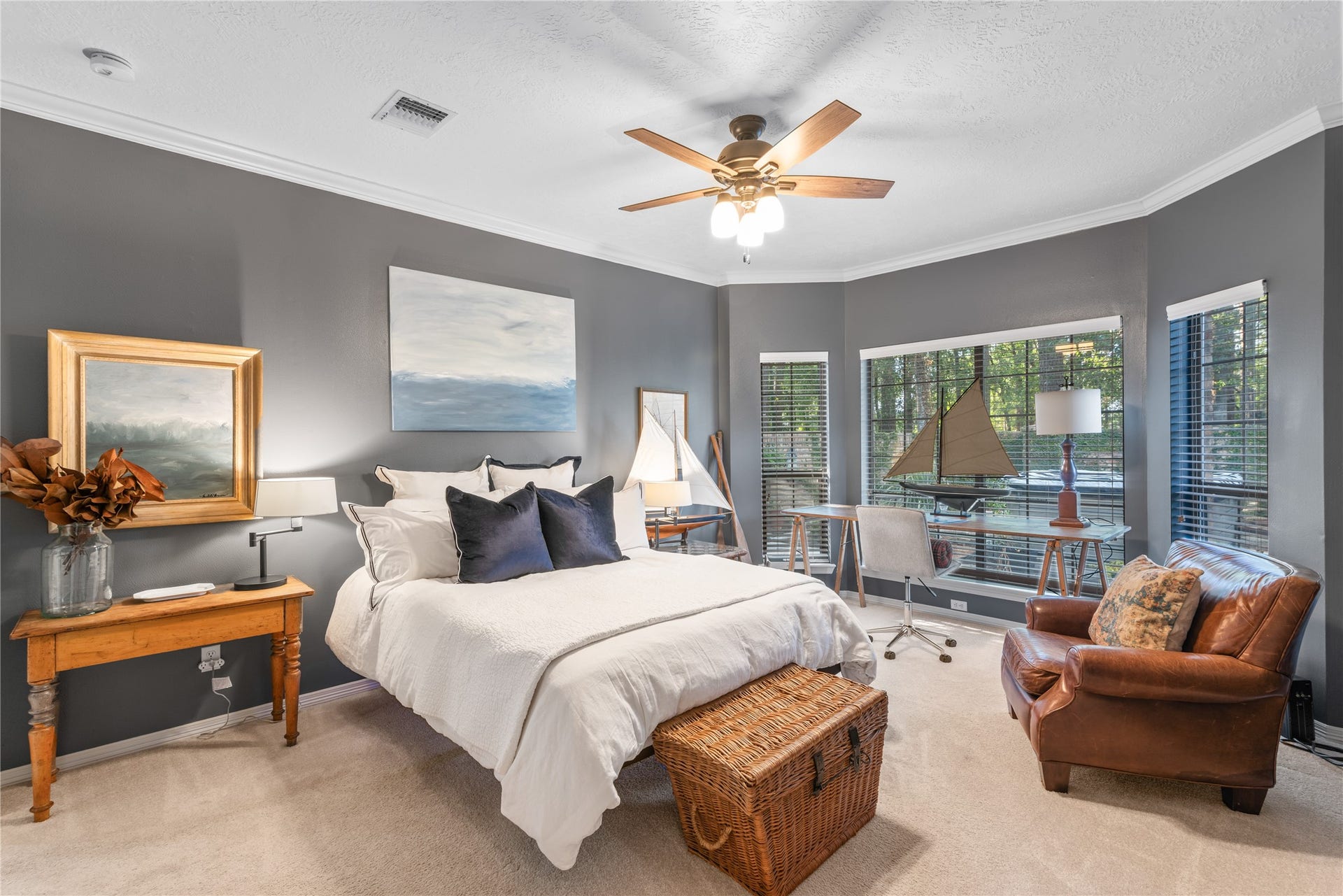 901 Longmire Road, #51, Conroe, TX 77304 One of Two Oversized spacious primary bedrooms with warm gray walls features a cozy bed, elegant wood furnishings, and a large window for natural light, complemented by a ceiling fan for comfort.
