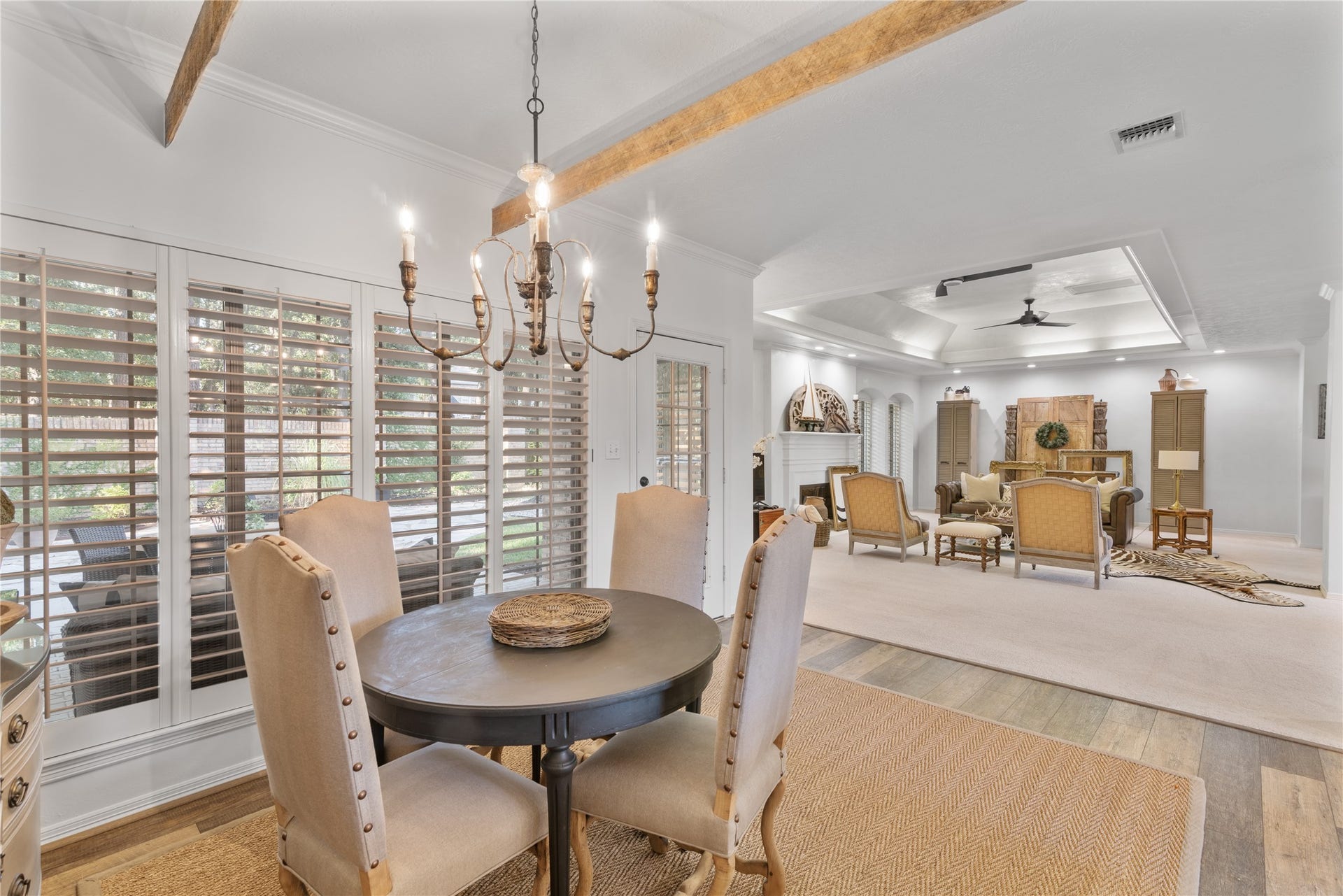 901 Longmire Road, #51, Conroe, TX 77304 A touch of charm and luxury with a chandelier over the spacious casual dining area opens to a spacious living room featuring a coffered ceiling and cozy seating, all bathed in natural light from large windows with wooden shutters.