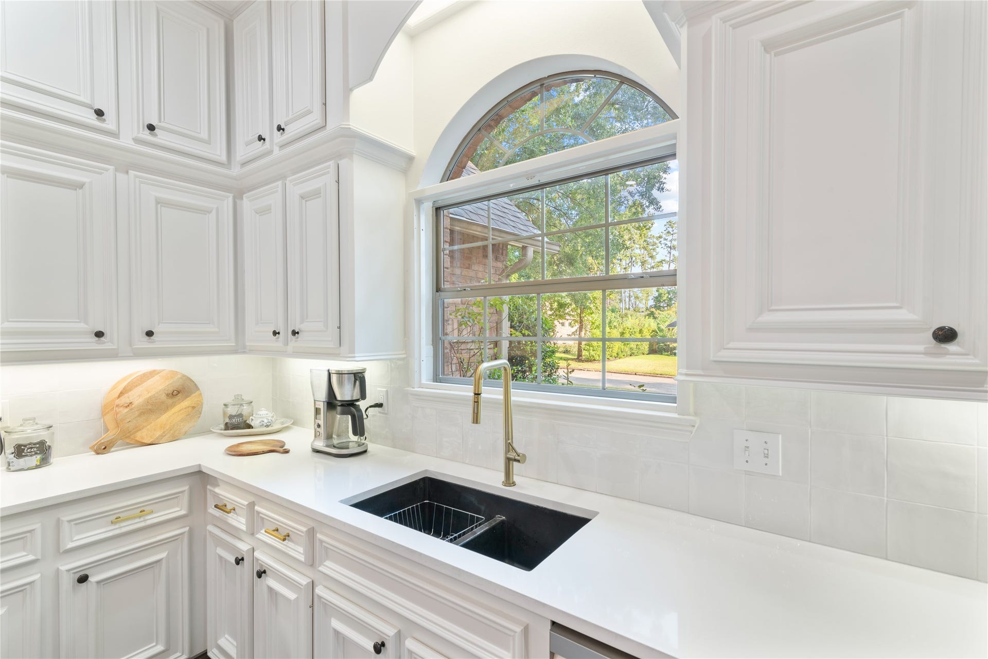 901 Longmire Road, #51, Conroe, TX 77304 Bright kitchen featuring elegant white cabinetry, a sleek undermount sink with a modern faucet, and a large arched window offering scenic views.
