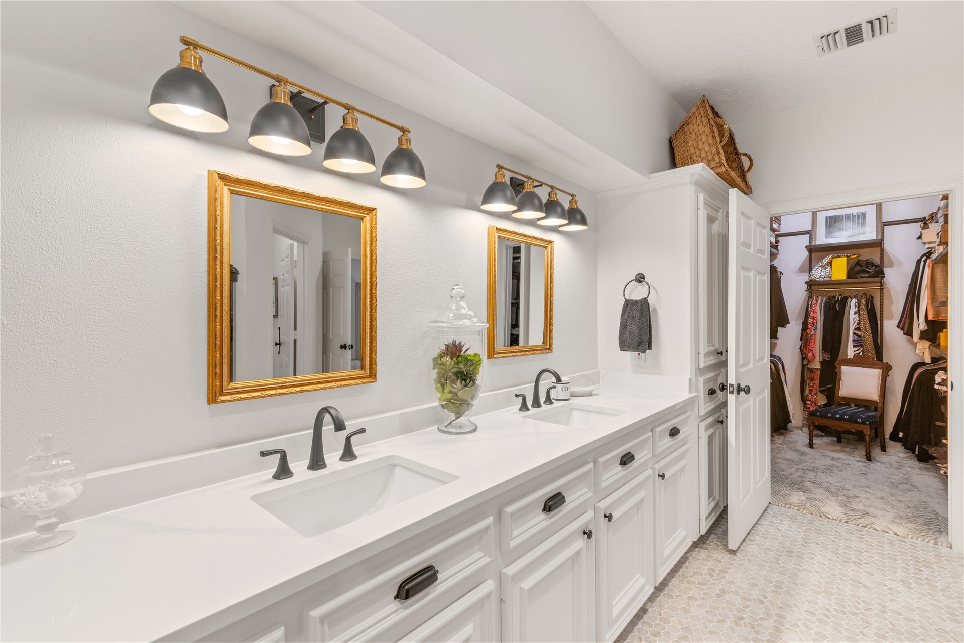 901 Longmire Road, #51, Conroe, TX 77304 Lots of storage in this large bathroom featuring dual sinks with sleek black fixtures, illuminated by stylish overhead lighting, and complemented by gold-framed mirrors. The space seamlessly leads into a spacious walk-in closet, offering ample storage and organization.