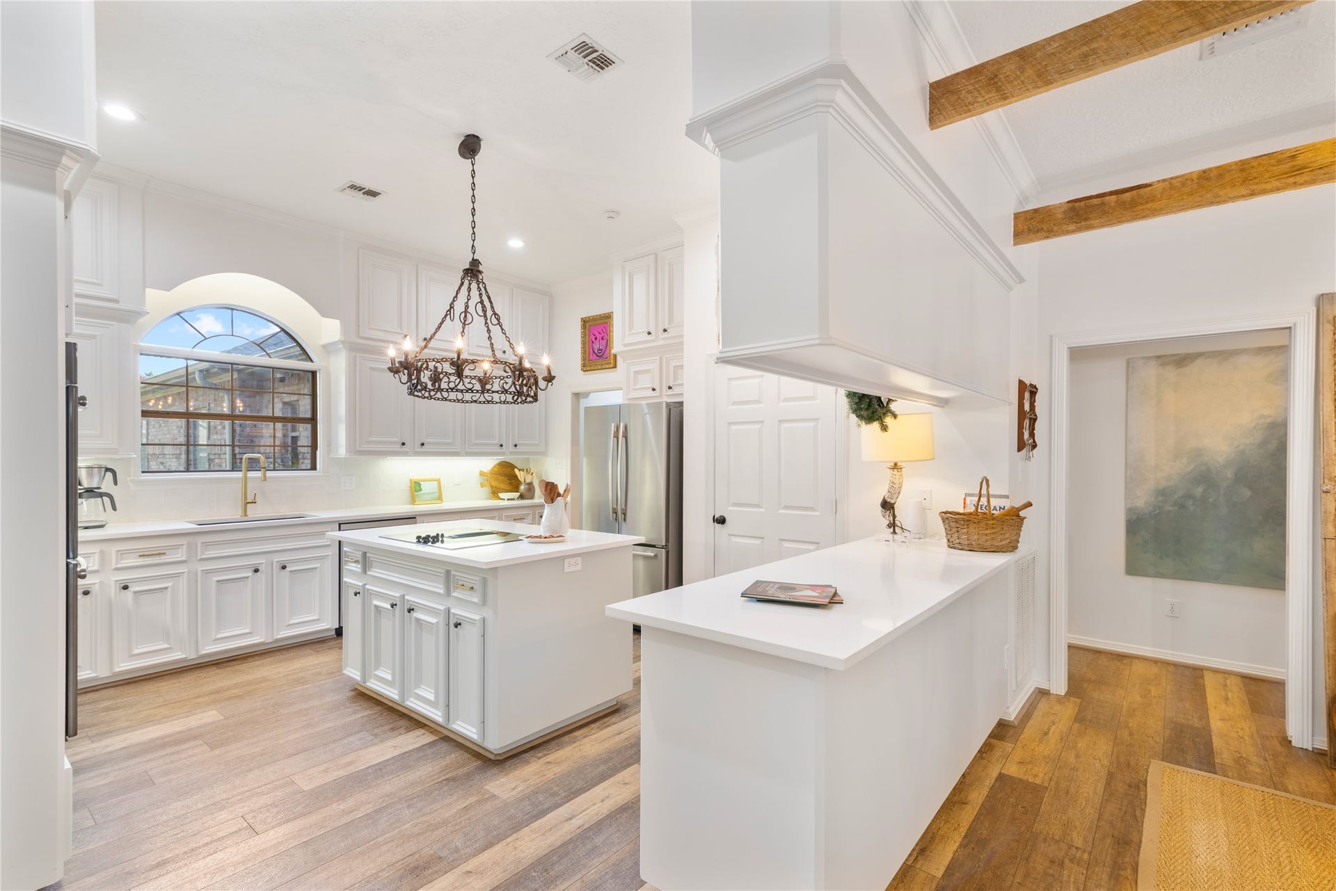 901 Longmire Road, #51, Conroe, TX 77304 Charming kitchen with elegant white cabinetry, a central island, and a stunning chandelier. The arched window and exposed wooden beams add character, while stainless steel appliances provide modern convenience.