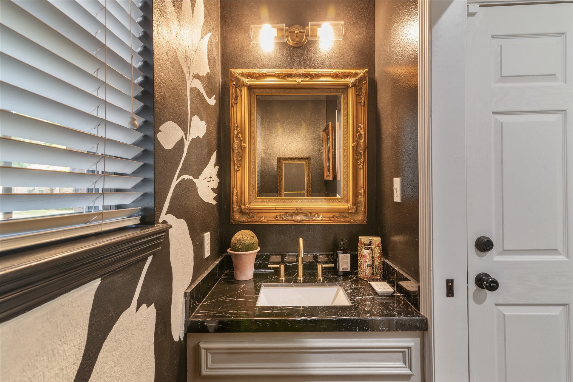 901 Longmire Road, #51, Conroe, TX 77304 Luxurious black marble countertop and a striking gold-framed mirror, complemented by artistic floral wall accents and modern lighting.