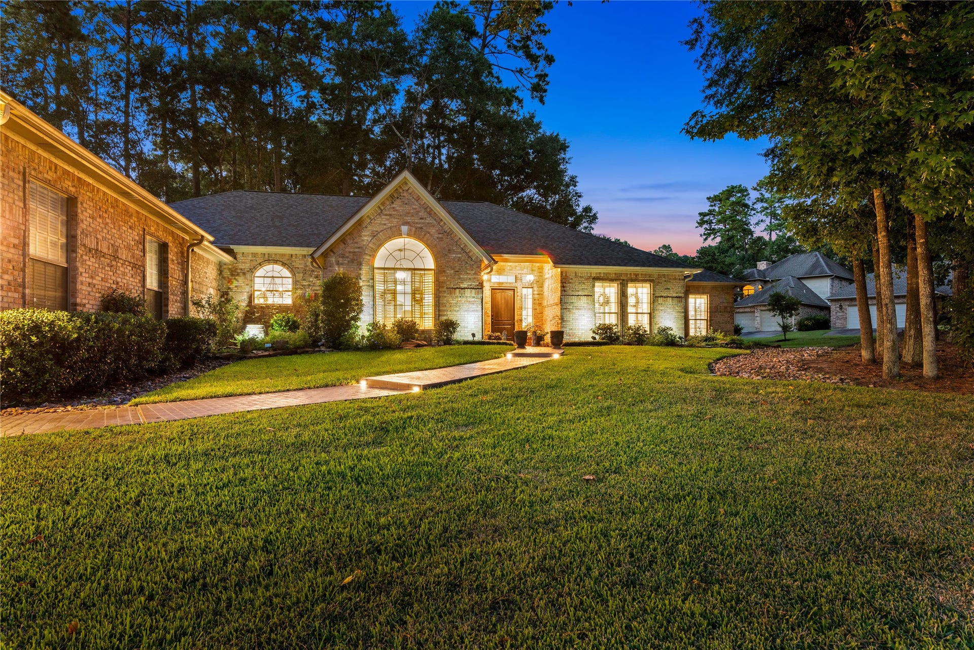 901 Longmire Road, #51, Conroe, TX 77304 Large solid brick home with elegant arched windows and a welcoming front path, set amidst lush landscaping and illuminated by warm exterior lighting.