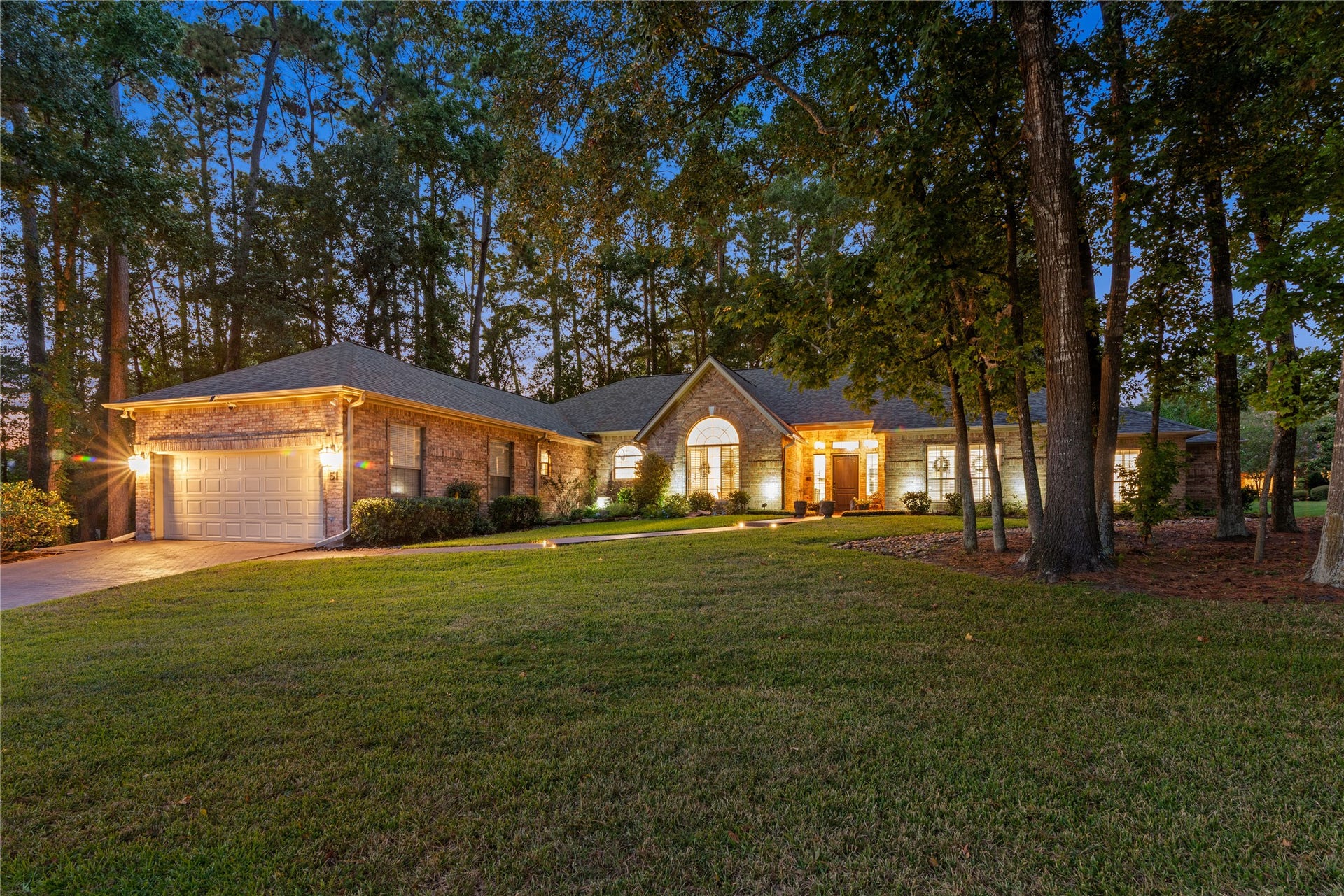 901 Longmire Road, #51, Conroe, TX 77304 Charming single-story brick home nestled among mature trees, featuring a spacious front yard and warm exterior lighting for a welcoming ambiance.