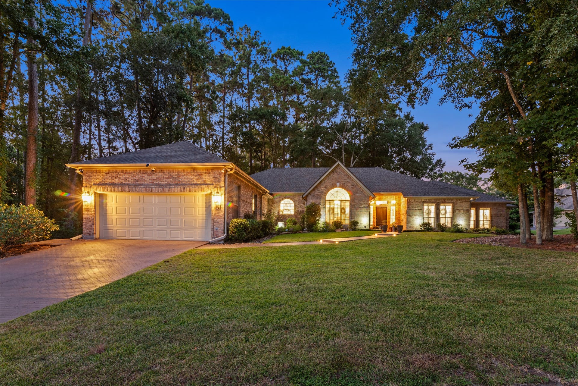 901 Longmire Road, #51, Conroe, TX 77304 Built to please with large rooms, great split floor plan with two primary bedrooms with sitting area and lots of room for privacy in this single-story brick home nestled among mature trees, featuring a spacious front yard and oversized lot and half with an inviting pathway, and warm exterior lighting for a welcoming ambiance.