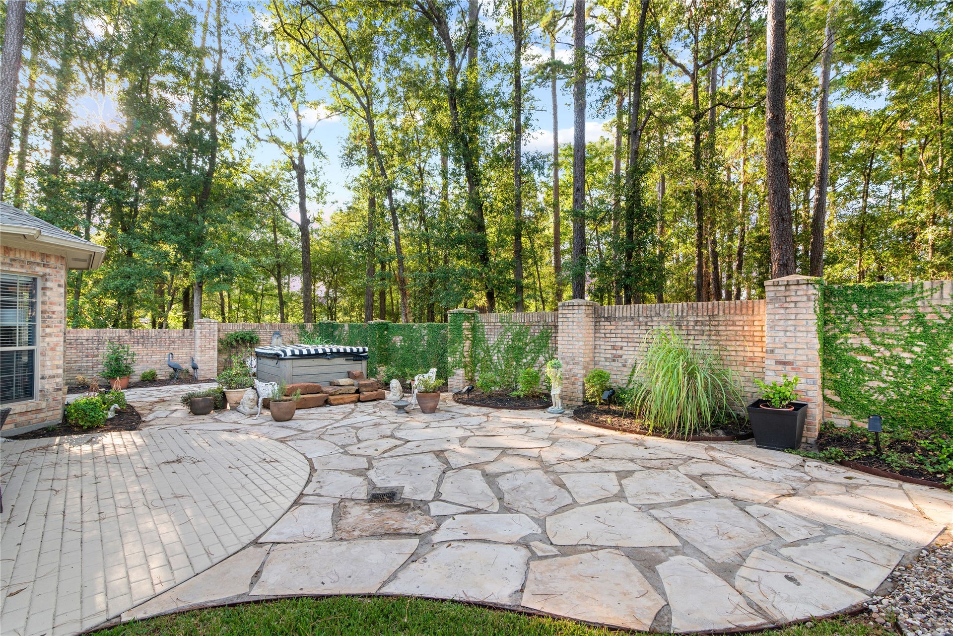901 Longmire Road, #51, Conroe, TX 77304 Serene backyard oasis with a spacious flagstone patio, surrounded by lush greenery and a charming brick wall for privacy. Perfect for relaxation and entertaining.