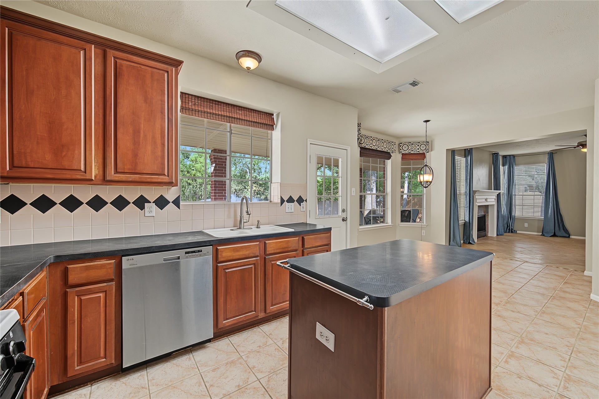 2302 Piney Woods Drive, Pearland, TX 77581 Island kitchen opens to the breakfast area, with the family room visible at the far end and backyard views through the windows