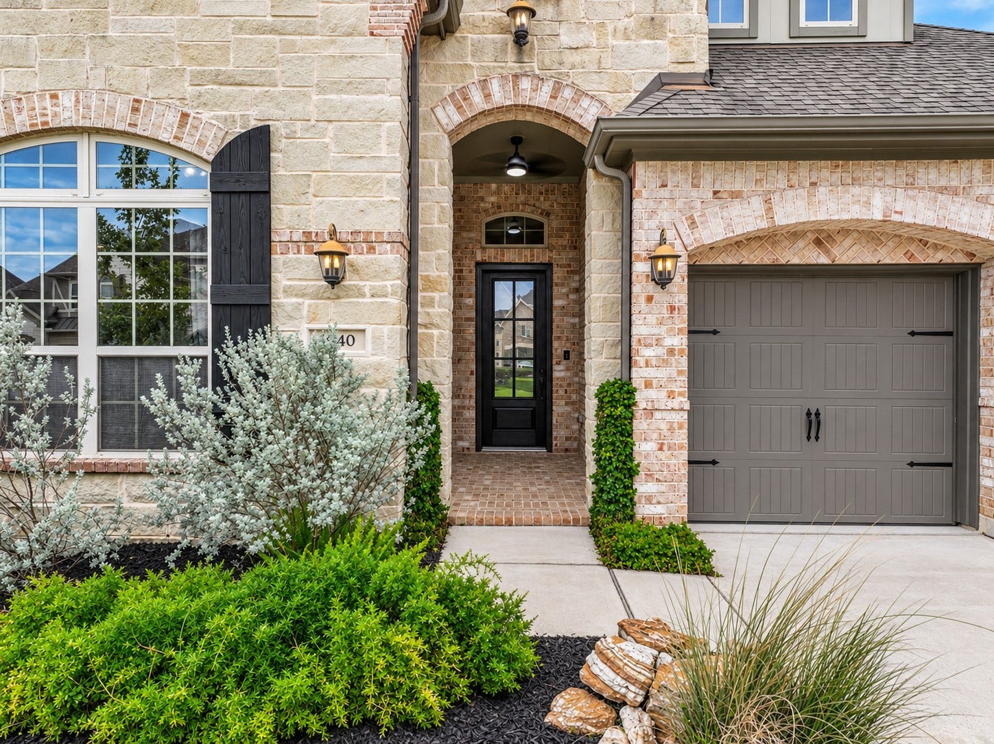 1640 Longwood Glen Lane, Friendswood, TX 77546 A closer look at the home's welcoming covered entry, framed by Austin limestone, decorative brick arches & attractive landscaping. Notice the carriage-style garage door, dark-stained wood shutter & brick-paved porch tucked beneath the impressive arched entrance.