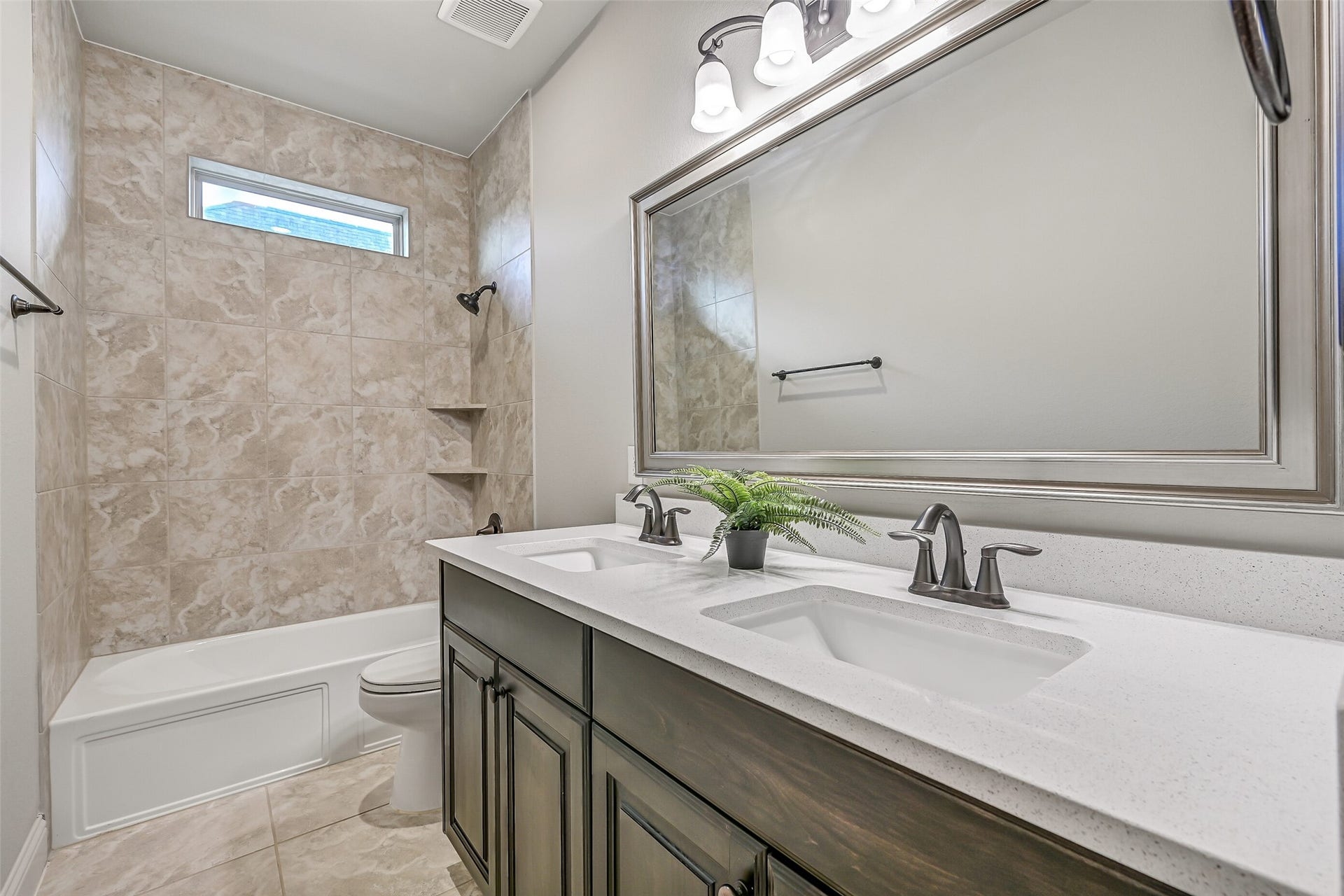 1640 Longwood Glen Lane, Friendswood, TX 77546 Situated between two secondary bedrooms, this full bath features a quartz countertop with dual rectangular sinks, stained wood cabinetry, a large framed mirror & a tub/shower combination with a tiled surround. A high-set window brings in natural light.
