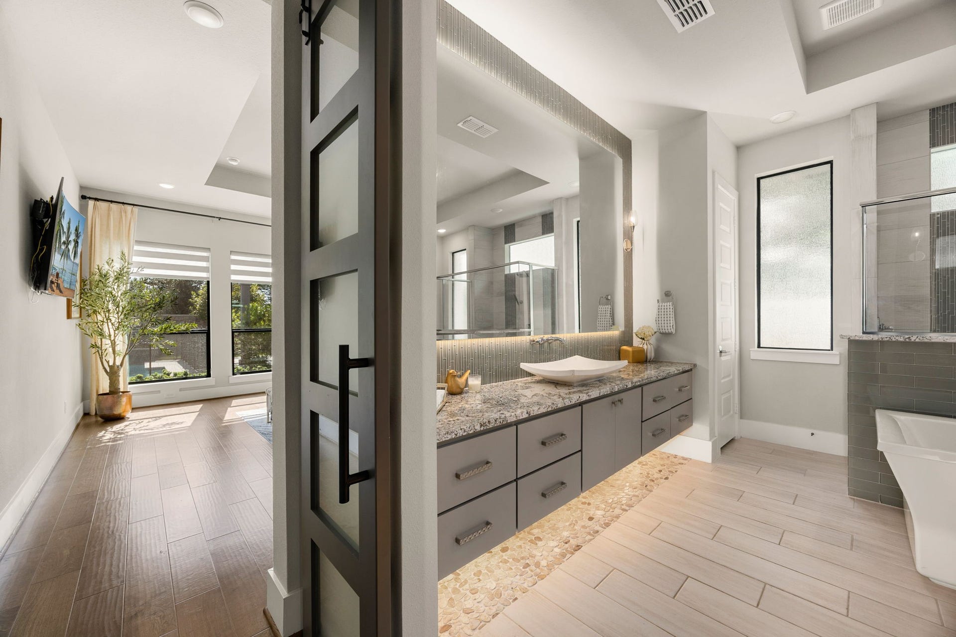 27927 Indigo Ridge Drive, Fulshear, TX 77441 Luxurious primary bathroom featuring a sliding barn door, dual floating vanities, elegant finishes with mirror lighting and floor lighting, and a spacious, spa-inspired design.