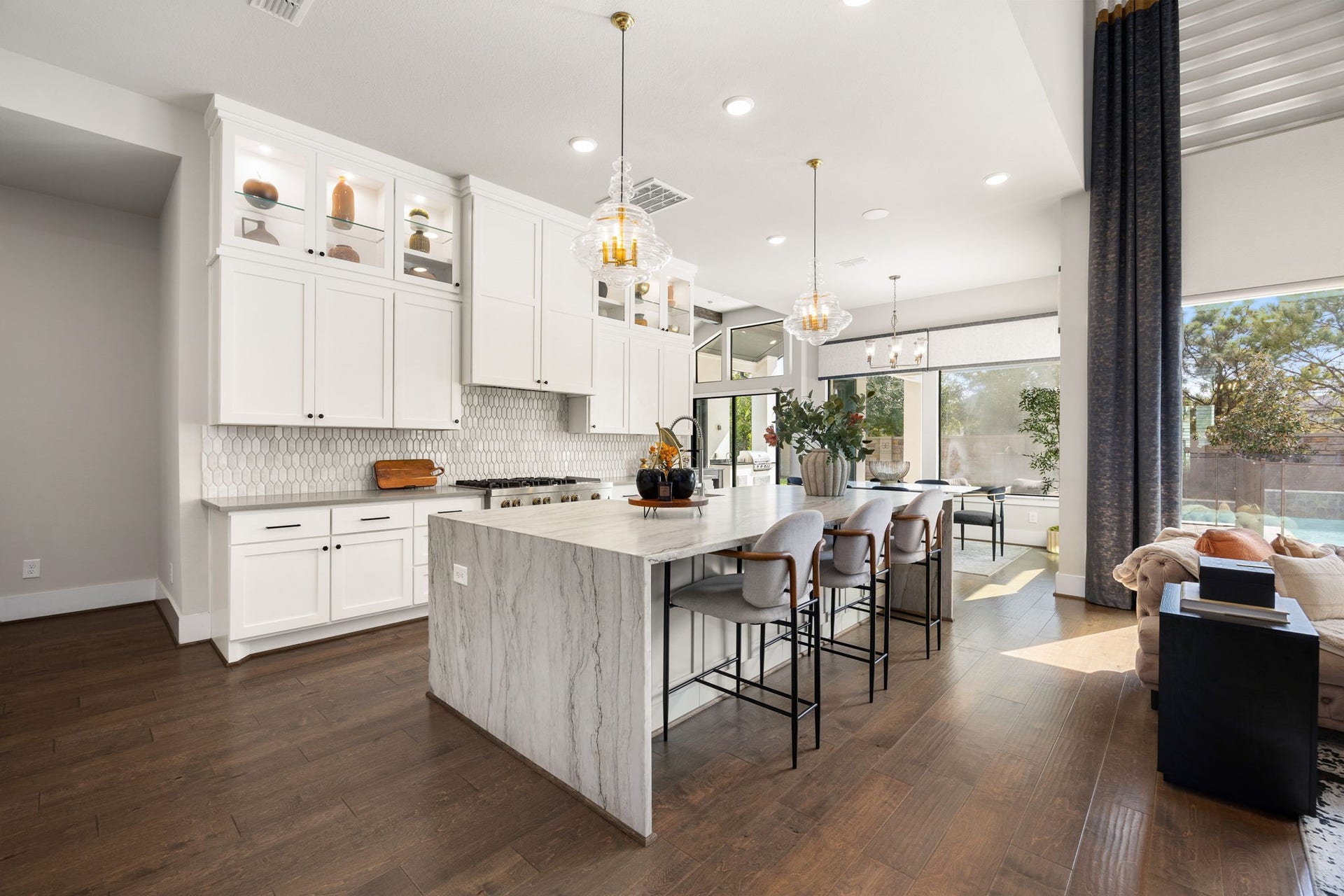 27927 Indigo Ridge Drive, Fulshear, TX 77441 Gorgeous gourmet kitchen featuring a large center waterfall quartzite island, beautiful cabinetry to the ceiling with glass doors and shelves, and an open layout ideal for entertaining.