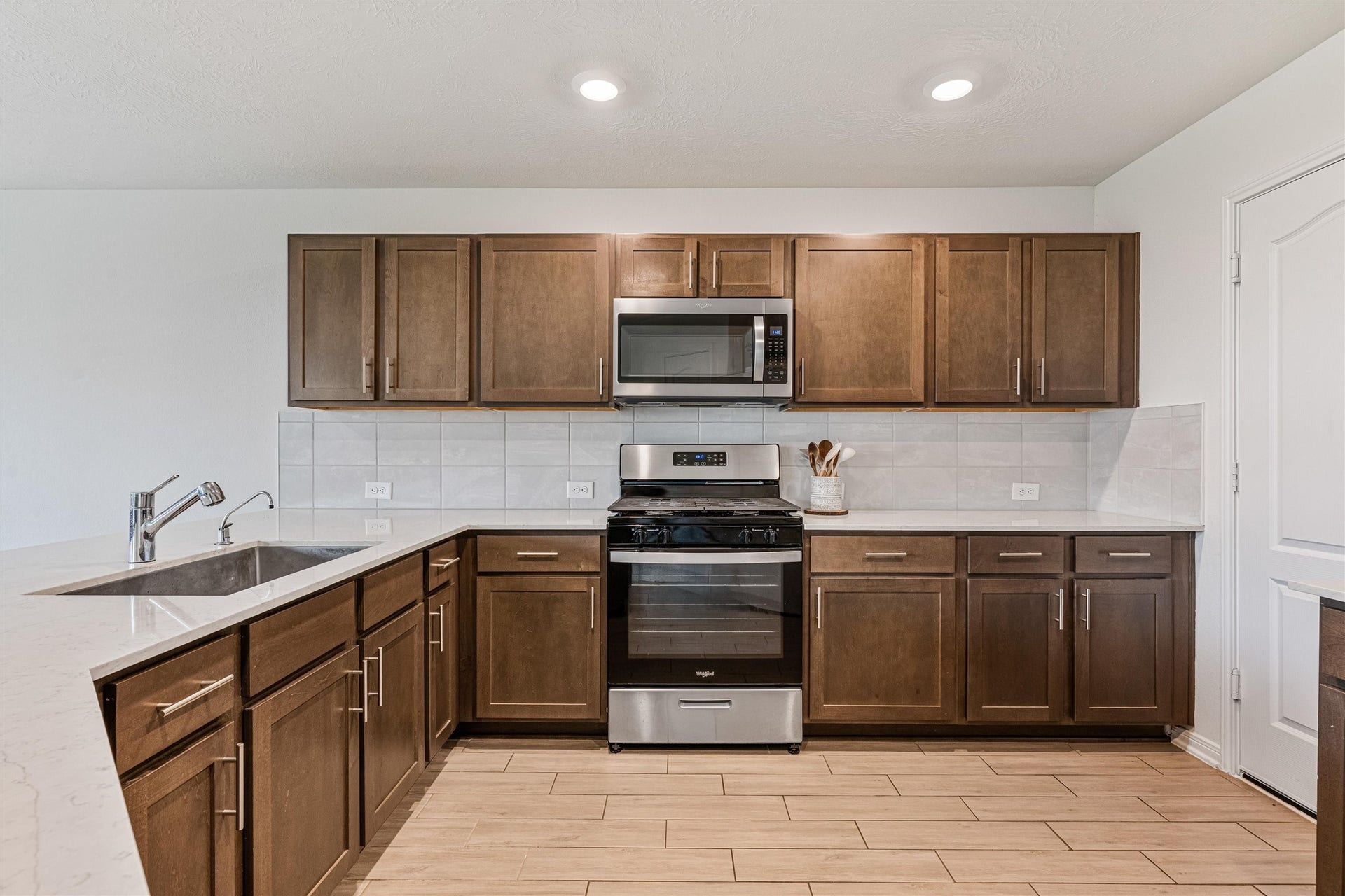 2873 Shimmer Edge Drive, Katy, TX 77493 Clean, symmetrical view of the kitchen showcasing abundant cabinetry, stainless steel appliances, and a gas range centered beneath a built-in microwave. The expansive counter space and continuous tile backsplash provide both functionality and a polished, cohesive design.