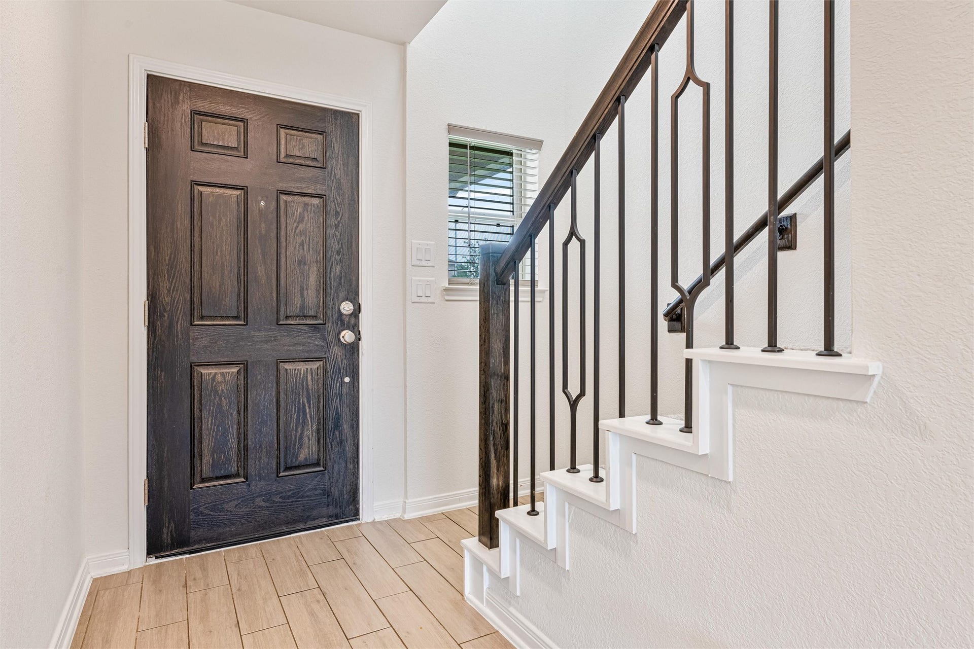 2873 Shimmer Edge Drive, Katy, TX 77493 Welcoming entry featuring durable wood-look tile flooring and a rich, paneled front door that creates a warm first impression. The staircase showcases crisp white risers paired with a stained wood handrail and decorative iron balusters.