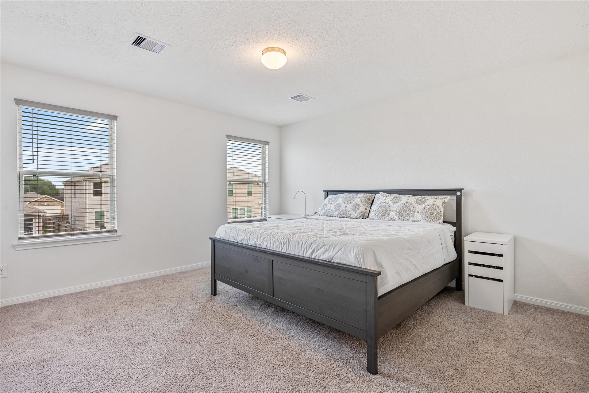 2873 Shimmer Edge Drive, Katy, TX 77493 Spacious primary suite offering a serene retreat with plush carpet, soft neutral tones, and abundant natural light from multiple windows. The generous layout easily accommodates a full bedroom set while maintaining an open, airy feel.