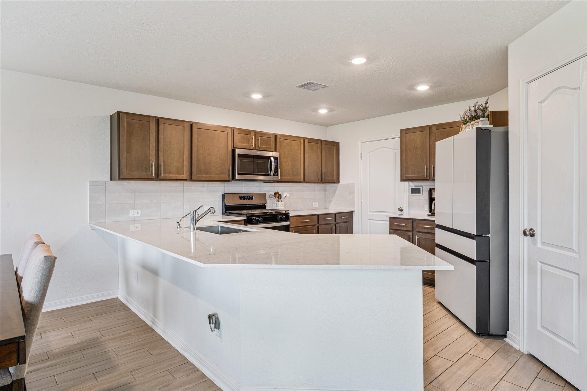 2873 Shimmer Edge Drive, Katy, TX 77493 Spacious kitchen anchored by an oversized wraparound breakfast bar with sleek quartz countertops, offering ample seating and prep space. The open layout overlooks the dining and living areas, while rich wood cabinetry, recessed lighting, and a neutral tile backsplash create a warm yet modern feel.
