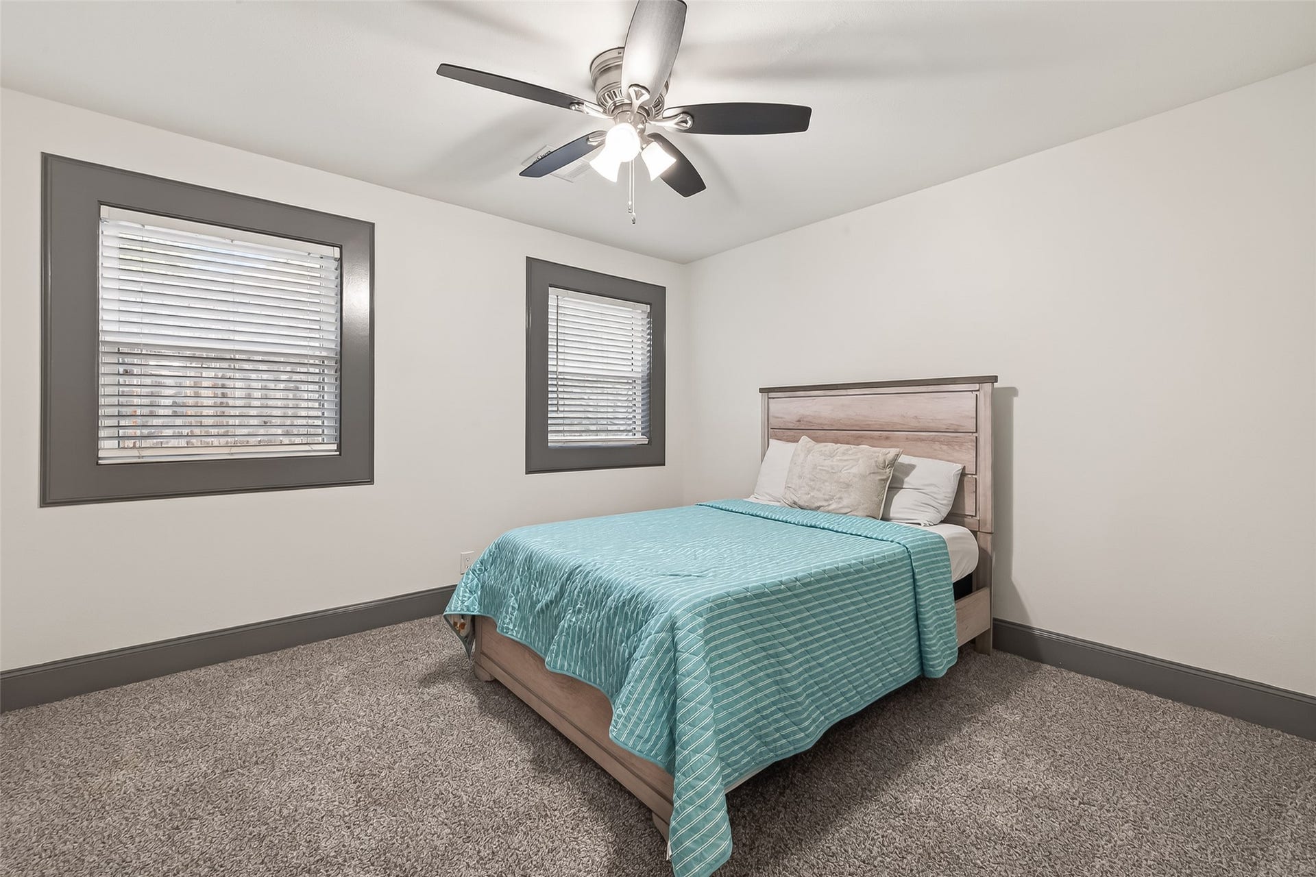10054 Cedardale Drive, Houston, TX 77055 This bedroom features neutral decor with gray trim, two windows for natural light, plush carpet, and a ceiling fan for comfort.