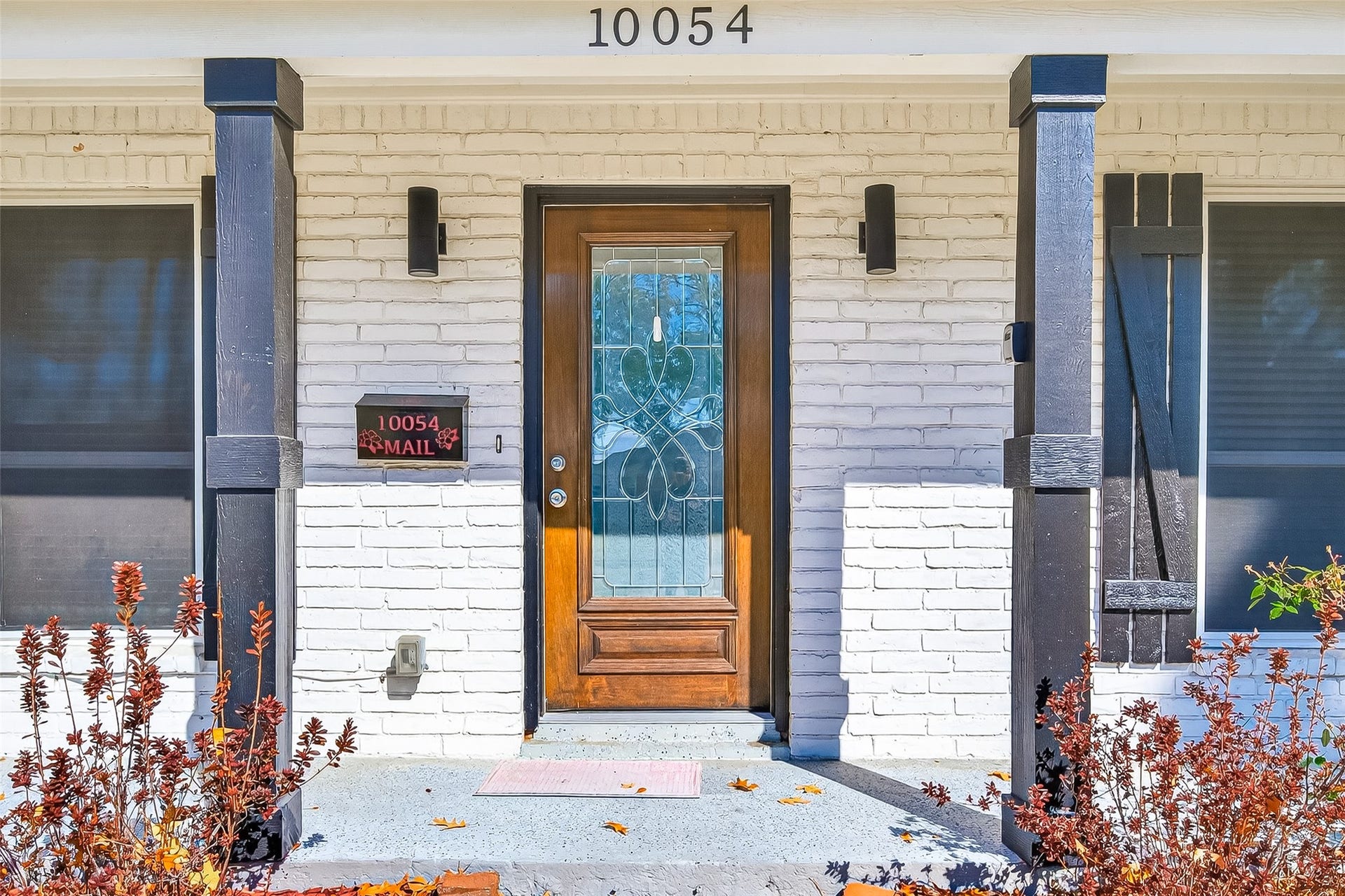10054 Cedardale Drive, Houston, TX 77055 Front entrance with a white brick facade, a decorative wooden door with glass detailing, and dark wooden columns.