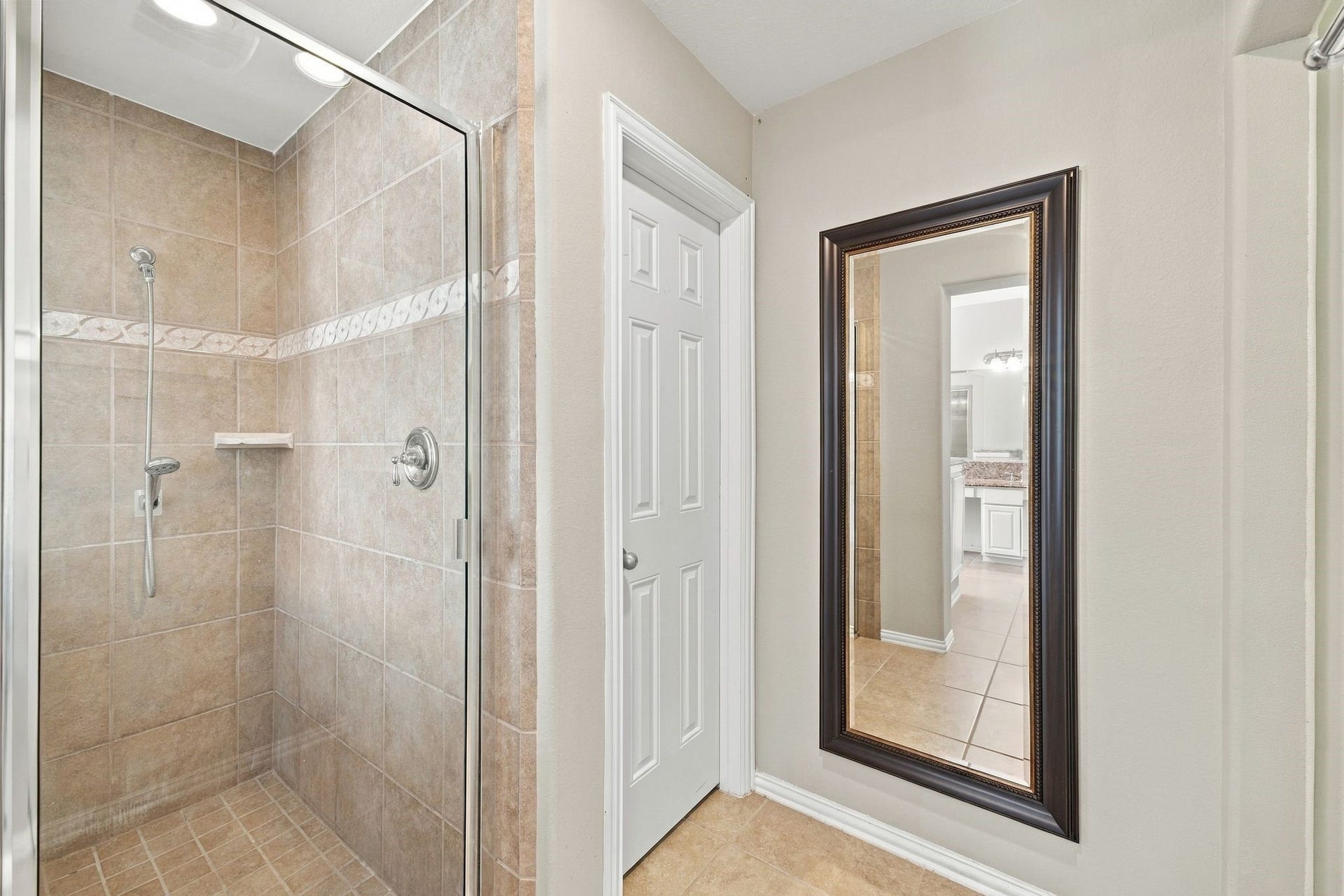 8319 Floating Heart Court, Conroe, TX 77385 Separate glass-enclosed shower with timeless neutral tile and natural light from the window overlooking the tub.
