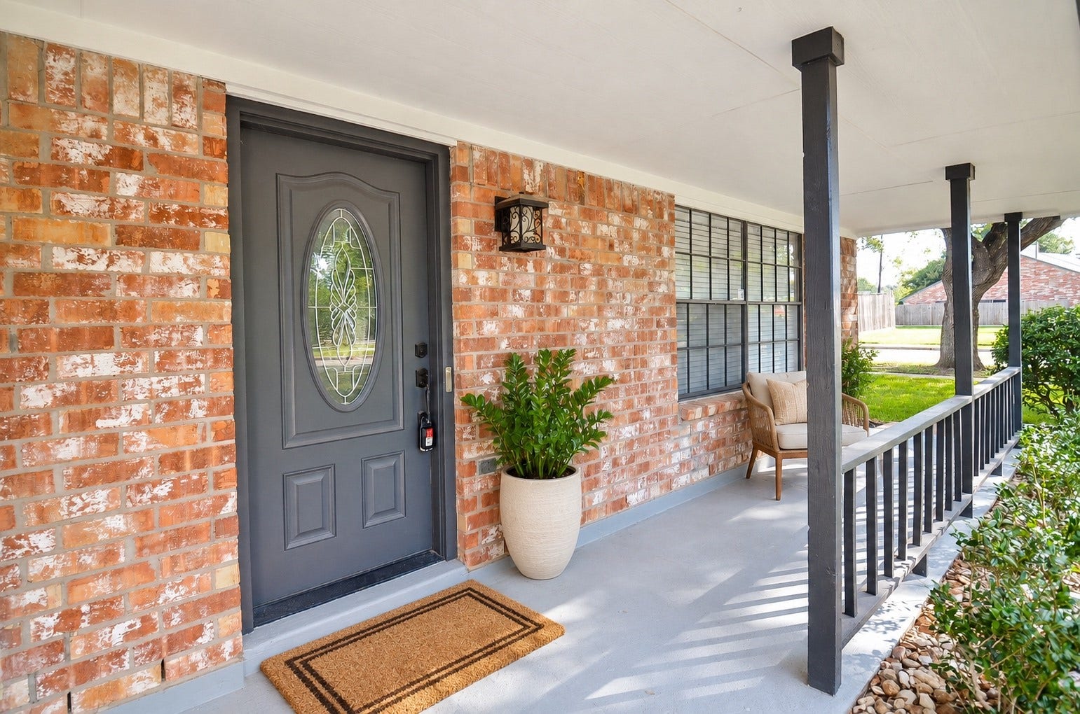 Inviting brick porch featuring a gray front door with decorative glass, comfortable seating, and timeless black railings.