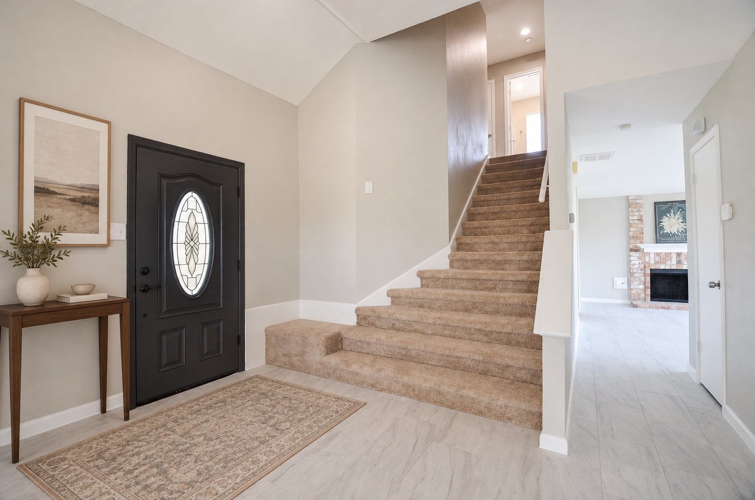 A bright, welcoming entryway showcases elegant tile flooring, a stylish front door, and a comfortable carpeted staircase. The open layout flows into a cozy living room, where a classic brick fireplace adds warmth and charm.