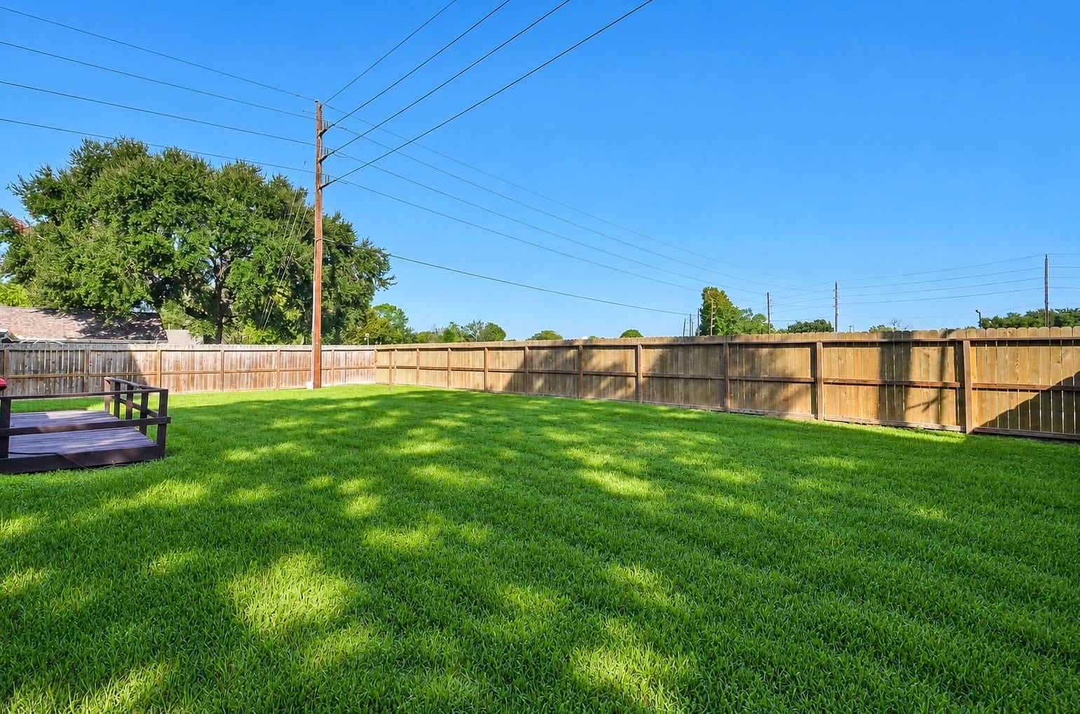 Expansive, sunlit backyard with lush green lawn, perfect for outdoor activities and relaxation, enclosed by a sturdy wooden fence for privacy.