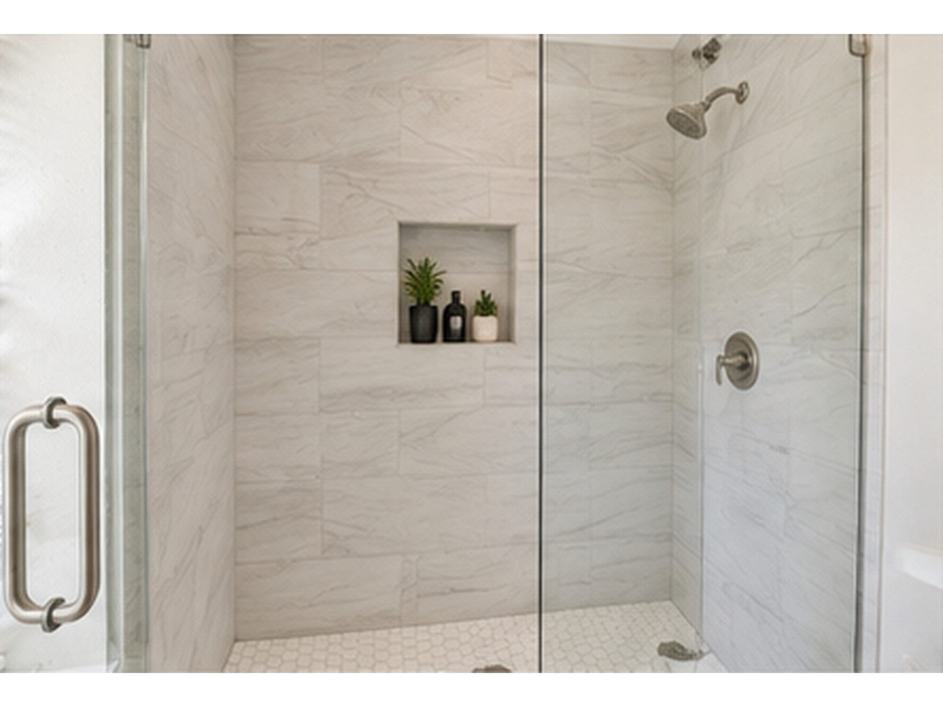 Indulge in the luxury of this elegant walk-in shower, boasting sleek glass doors, modern fixtures, a convenient built-in niche, and stylish tilework.