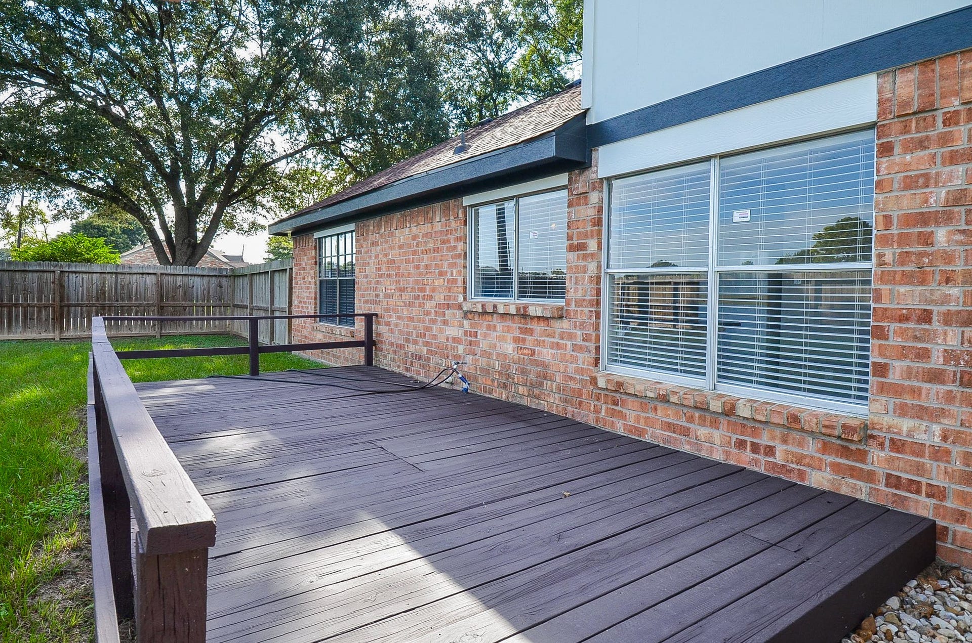 Charming brick exterior with large windows opens to a spacious wooden deck, perfect for outdoor entertaining, set in a private fenced yard.