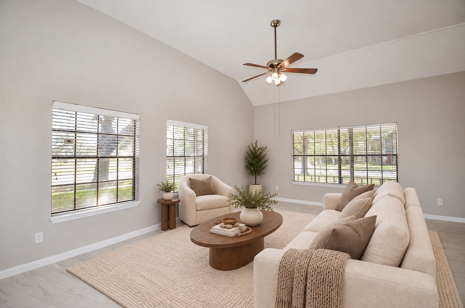 Airy living space with soaring ceilings, soft neutral tones, and elegant tile flooring. Large windows fill the room with natural light, while a ceiling fan adds everyday comfort.