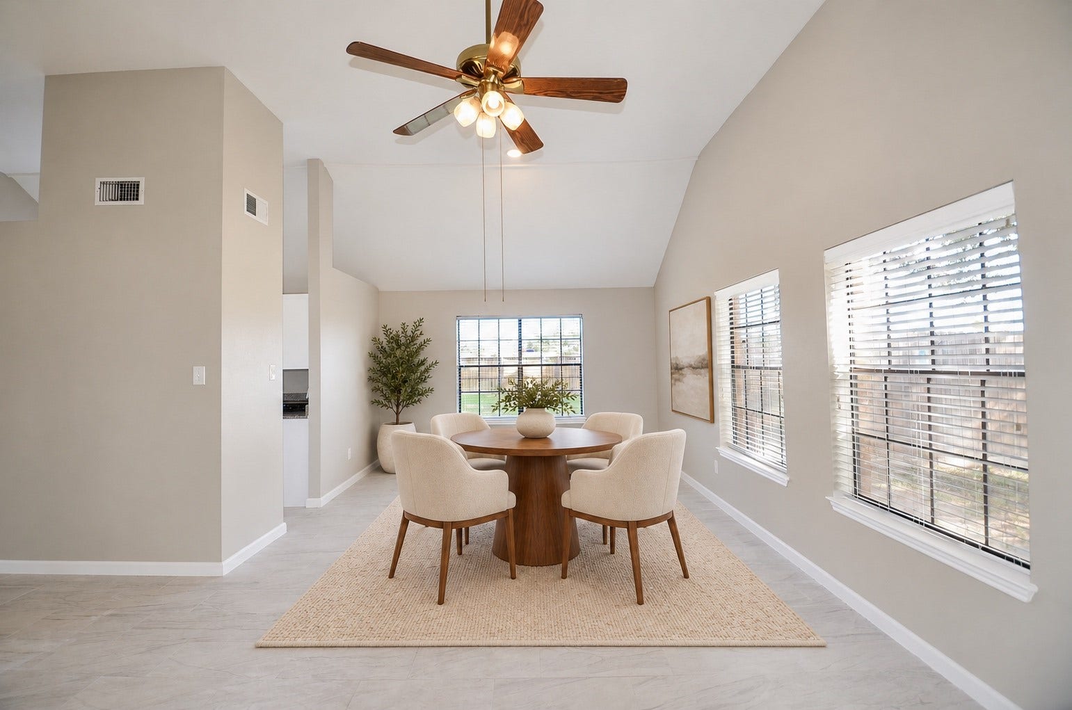 Spacious living area with high ceilings, neutral tones, and abundant natural light from large windows, complemented by a stylish ceiling fan.
