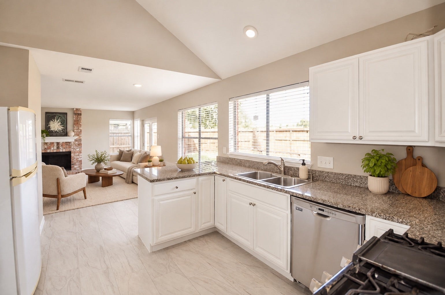 Bright and airy kitchen with modern appliances and granite countertops flows seamlessly into a cozy living area with a brick fireplace, perfect for entertaining or relaxing.