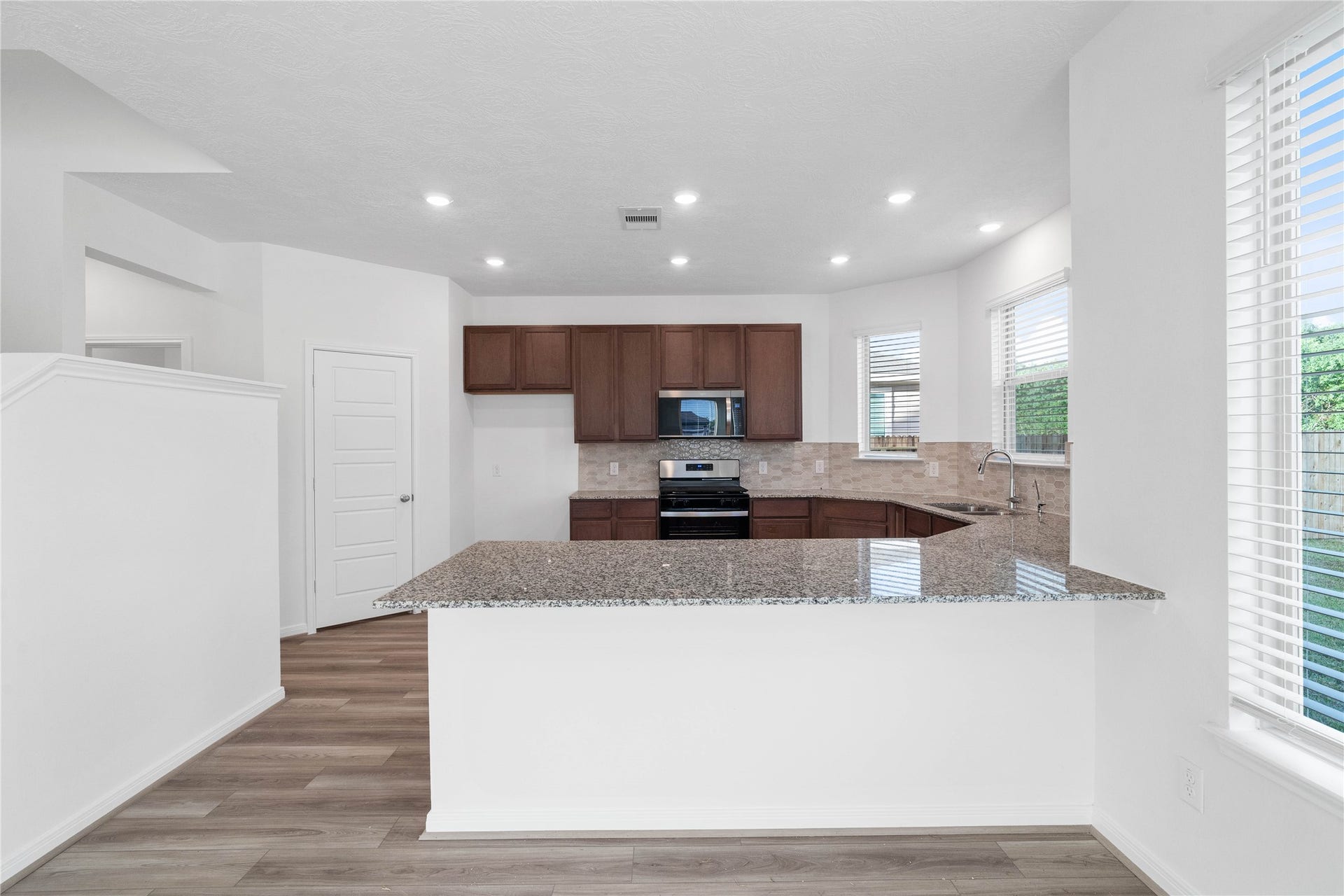 5623 Blackbird Lane, Hitchcock, TX 77563 The kitchen features rich ginger stained wood cabinetry, granite countertops, and a pearl colored picket mosaic backsplash that adds subtle texture and style. Warm wood look flooring and natural light create an inviting space for everyday cooking and gathering.