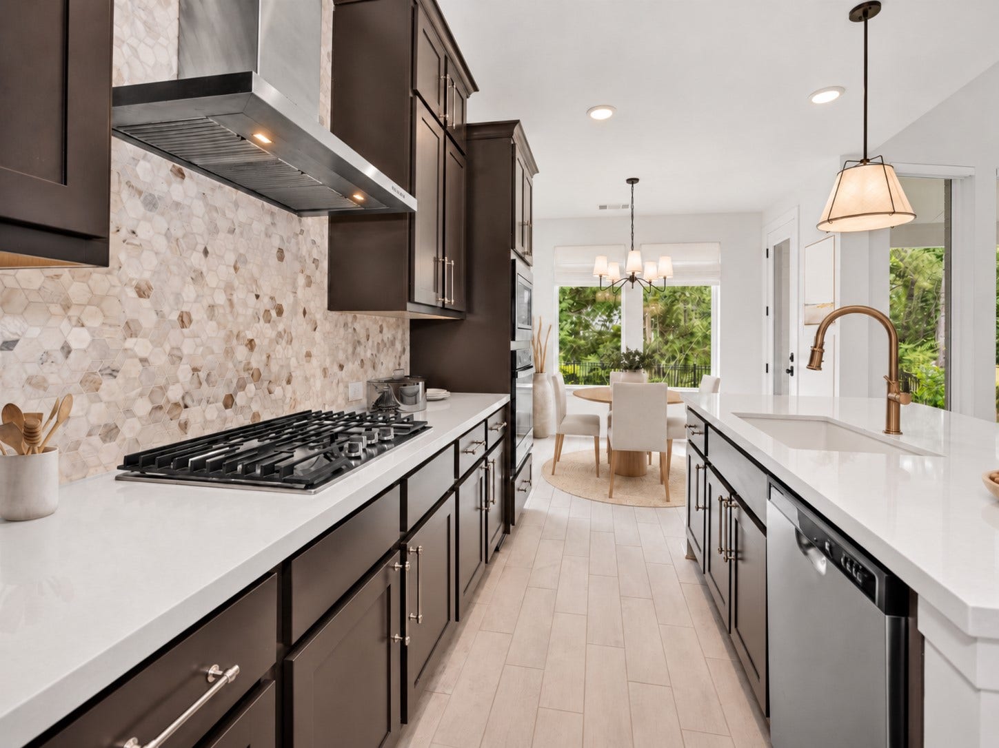 Designer kitchen showcasing warm, rich cabinetry with select upper cabinets, upgraded vent hood, custom hardware, upgraded top-level backsplash, and elevated designer lightingcreating a timeless blend of warmth, sophistication, and function.